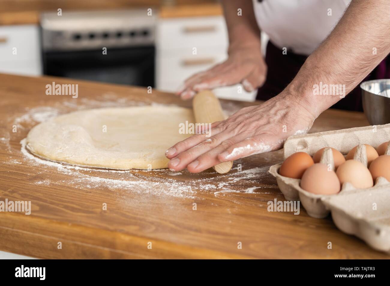 Mann, der Bäckerei in der Küche und rollt Teig auf der hölzernen Schneidebrett mit Mehl bedeckt Stockfoto