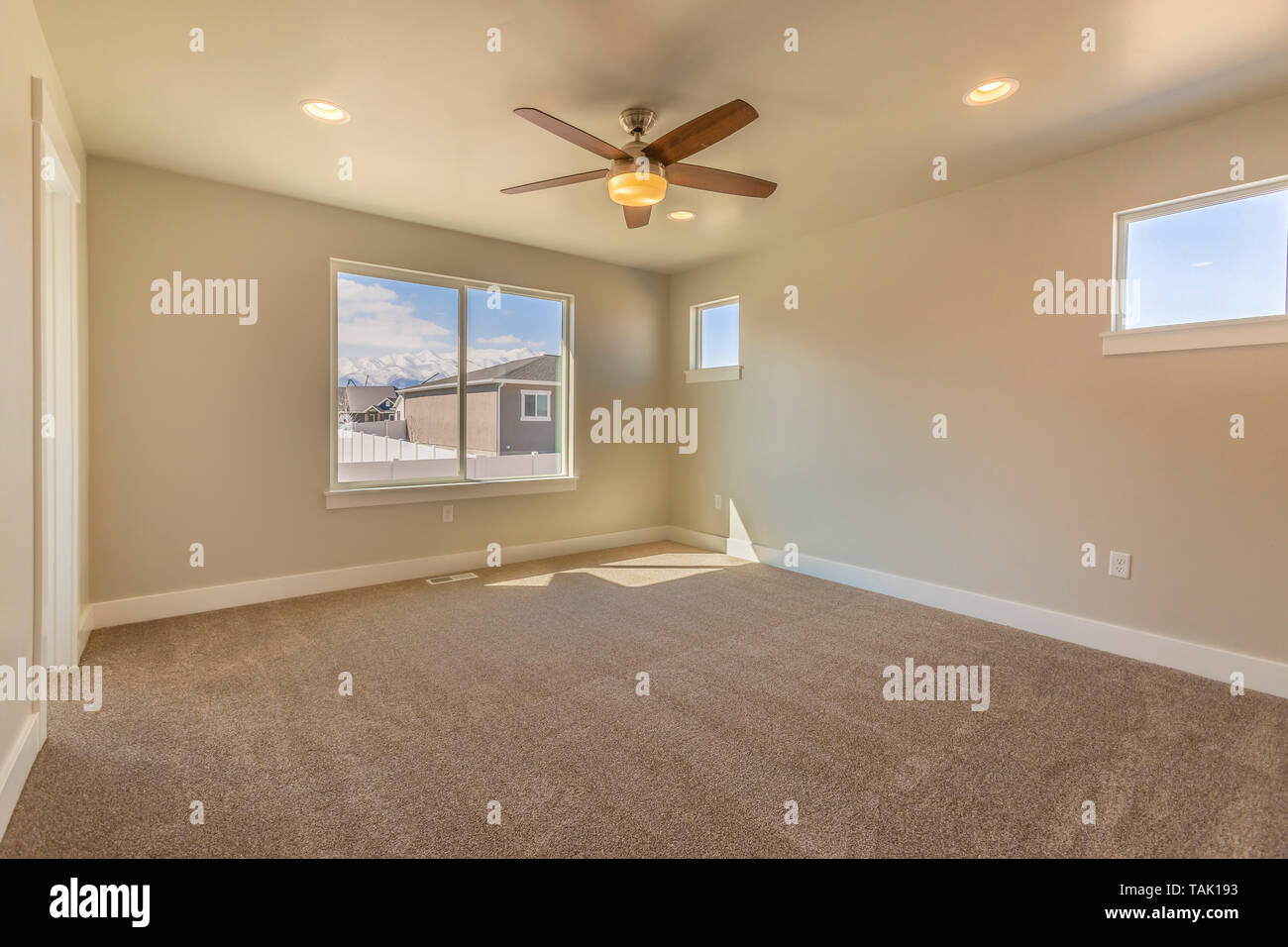 Leeren Raum von einem neuen Haus mit beige Wandfarbe und Teppichboden. Ein Lüfter befindet sich an der Decke und das Sonnenlicht durch die Fenster montiert. Stockfoto