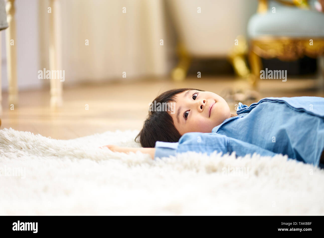 Süße kleine asiatische Junge lag auf dem Rücken auf dem Teppich im Wohnzimmer sah lächelnd Stockfoto
