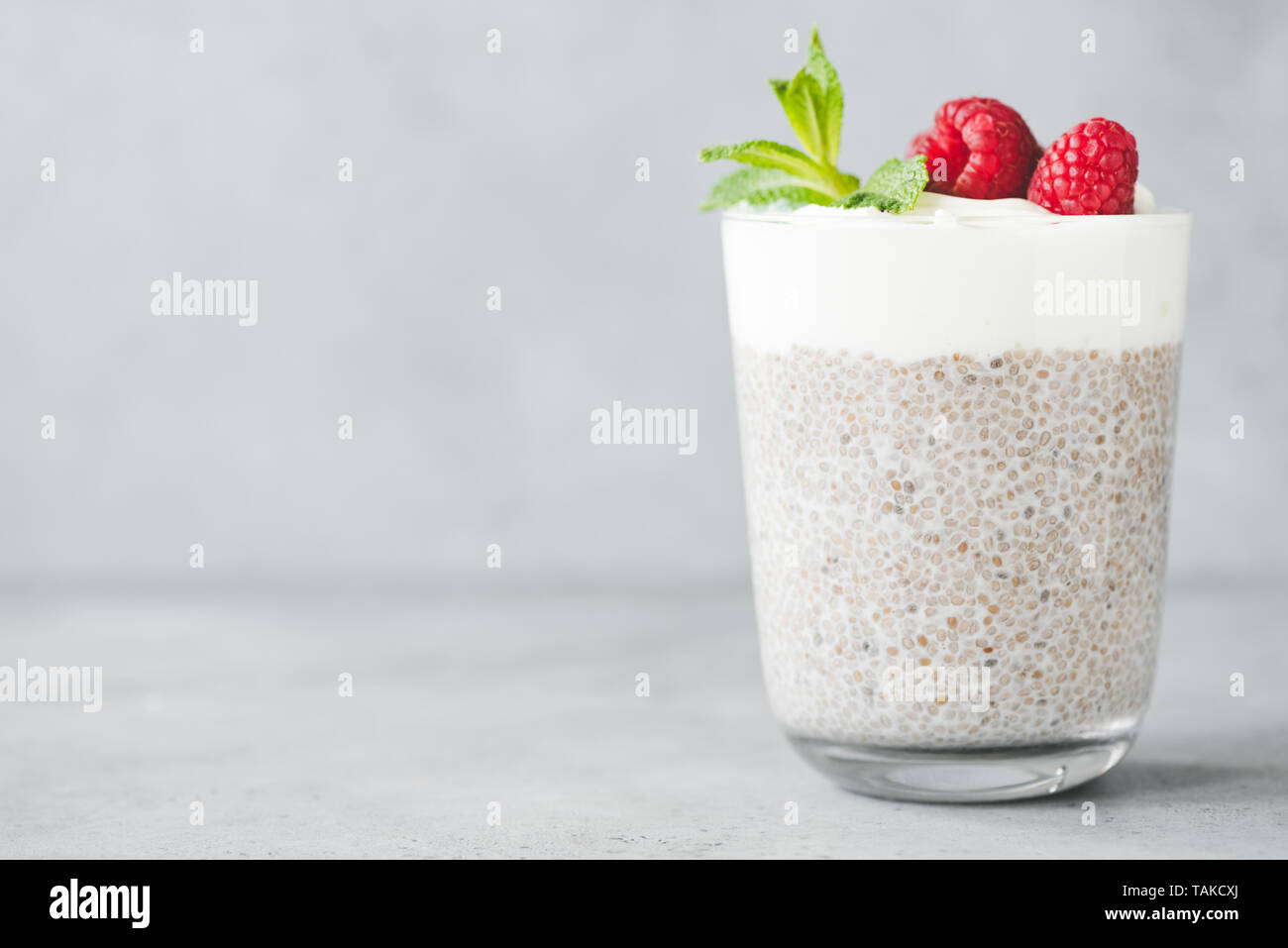 Chia Pudding mit Joghurt mit Himbeeren im Glas auf konkreten Hintergrund. Kopieren Sie Platz für Text. Konzept der gesunden Ernährung, gesunde und vegetarische lifes Stockfoto