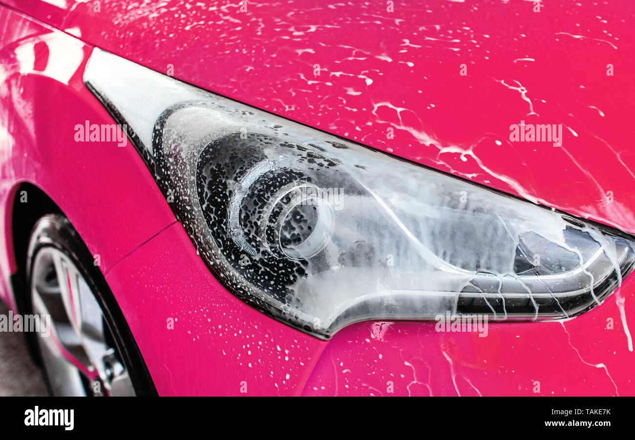 Rosa Auto vorne Licht im selbst gewaschen dienen Carwash, weiß Shampoo Schaum fließt auf Glas Stockfoto