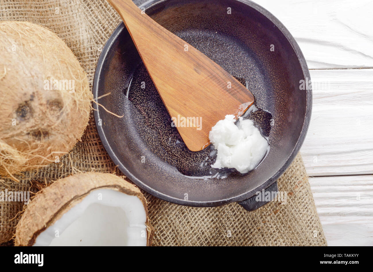 Kokosnuss, Shell mit Fleisch, Gusseisen Skillet und Spachtel auf Hanf Sack auf weißen Küche aus Holz Tisch Stockfoto