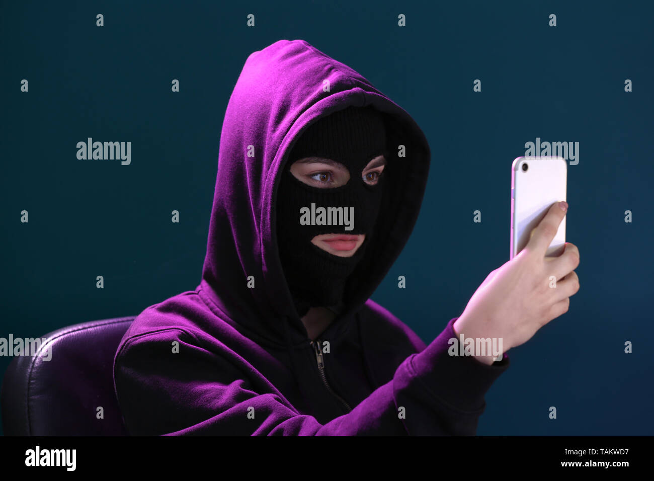 Weibliche Hacker in Maske und mit Mobiltelefon auf farbigen Hintergrund Stockfoto