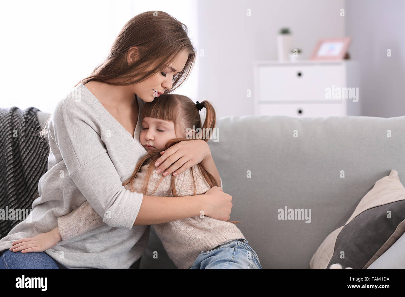 Traurige Frau nach Scheidung umarmte ihre kleine Tochter beim Sitzen auf dem Sofa Stockfoto
