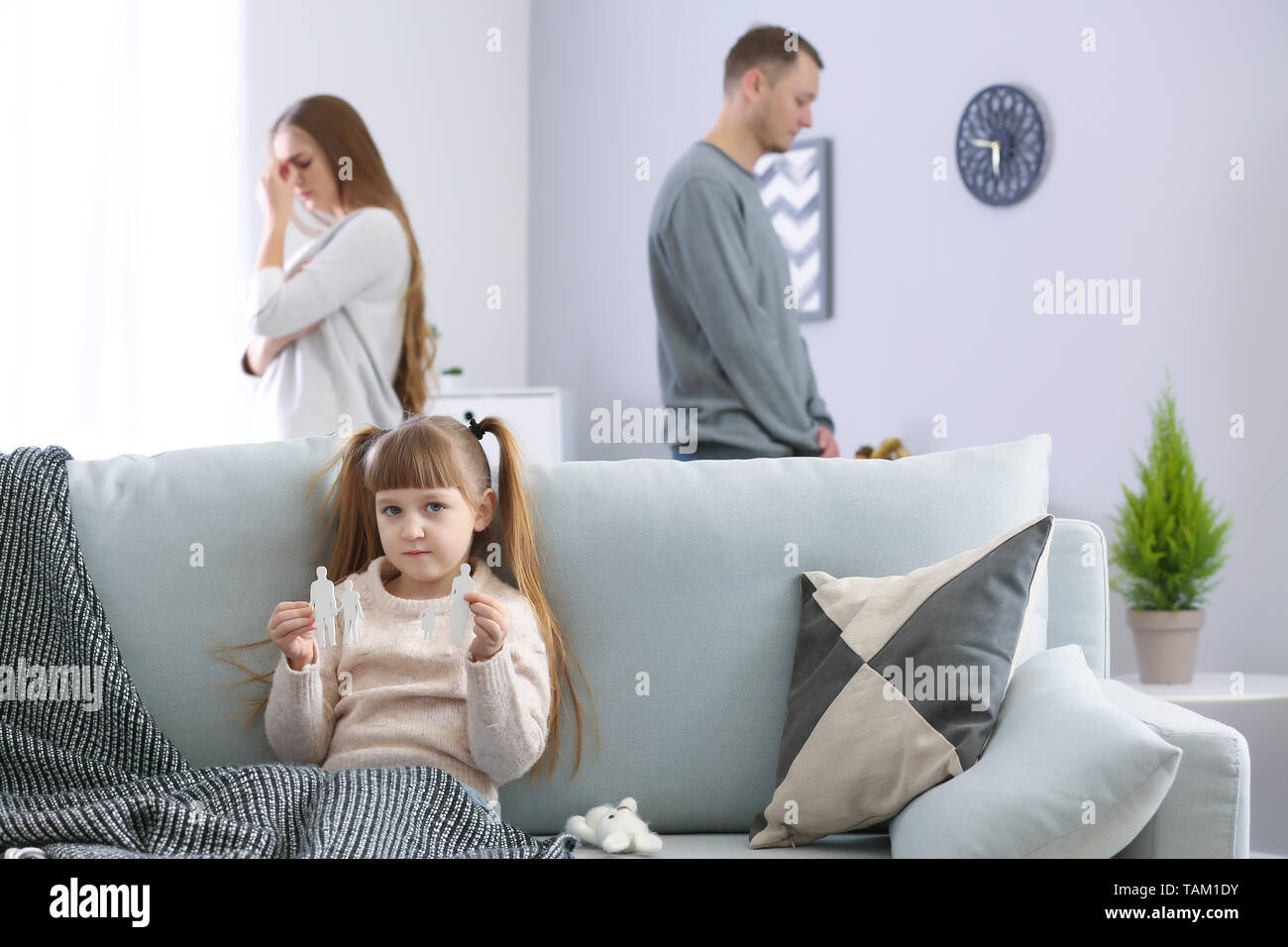 Trauriges kleines Mädchen mit gebrochenen Figur der Familie sitzt auf dem Sofa, während ihre Eltern zu Hause streiten. Konzept der Scheidung Stockfoto