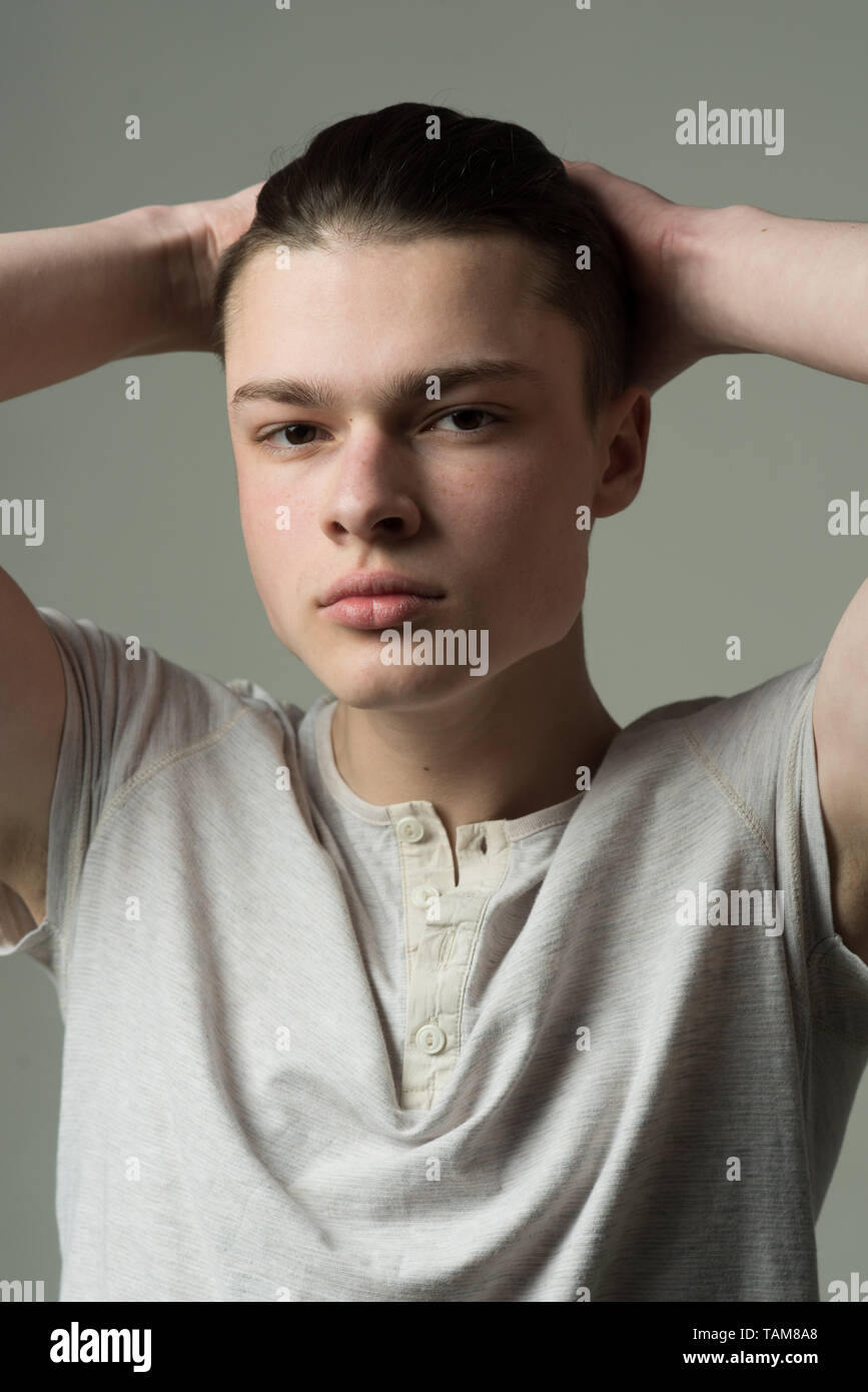 Kerl auf zuversichtlich Gesicht in Light shirt berührt Haar, grauen Hintergrund. Macho mit stilvollen lange Haare schneiden. Friseur- und Frisur Konzept. Glatter Mann ski Stockfoto