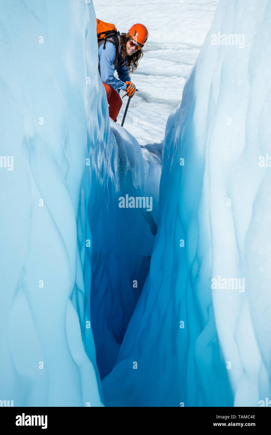 Ein Gletscher in Orange und Blau lehnt sich über eine tiefe schmale Gletscherspalte auf einem Gletscher in Alaska zu prüfen. Stockfoto