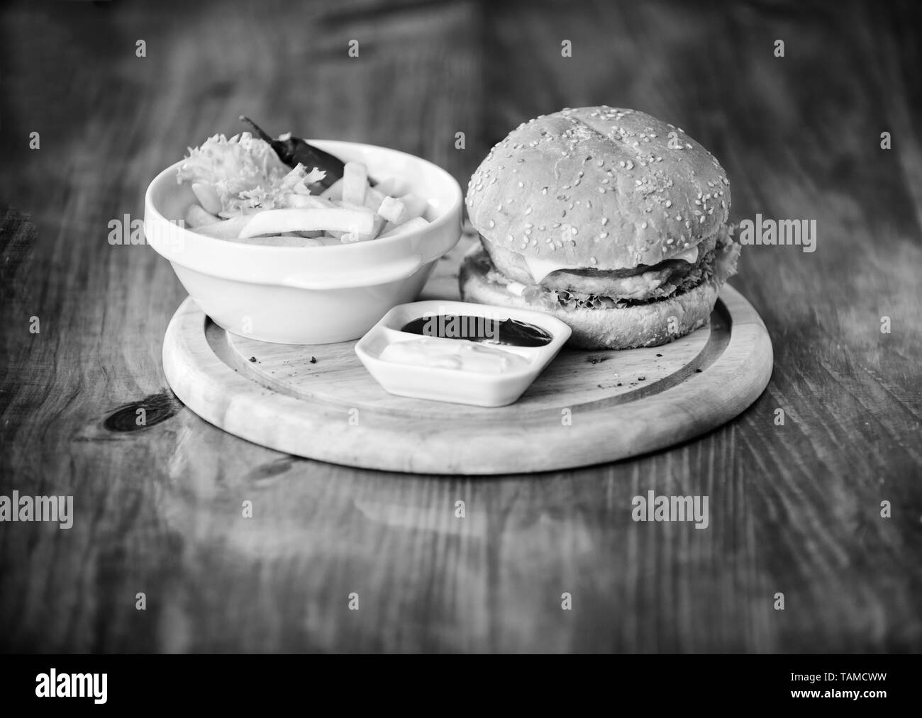 Burger mit Käse, Fleisch und Salat. Cheat meal. Leckere Burger mit Sesam. Fast food Konzept. Burger Menü. Kalorienreiche Snacks. Hamburger und Pommes frites und Tomatensauce auf Holzbrett. Stockfoto