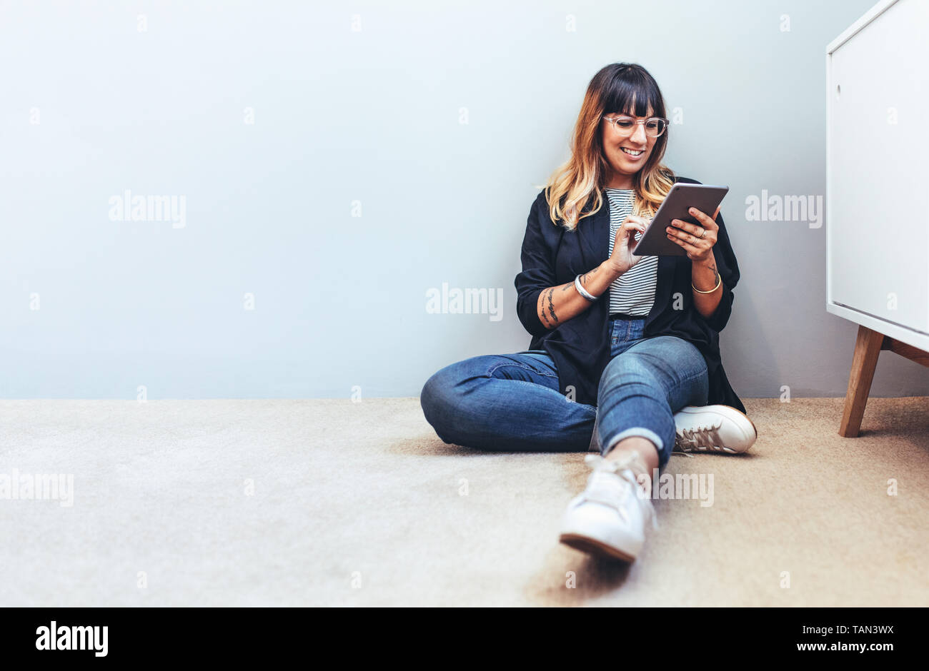 Lächelnde Frau sitzt auf dem Boden mit einem Tablet-PC. Entspannt Geschäftsfrau ihre Mails auf einem Tablet PC. Stockfoto