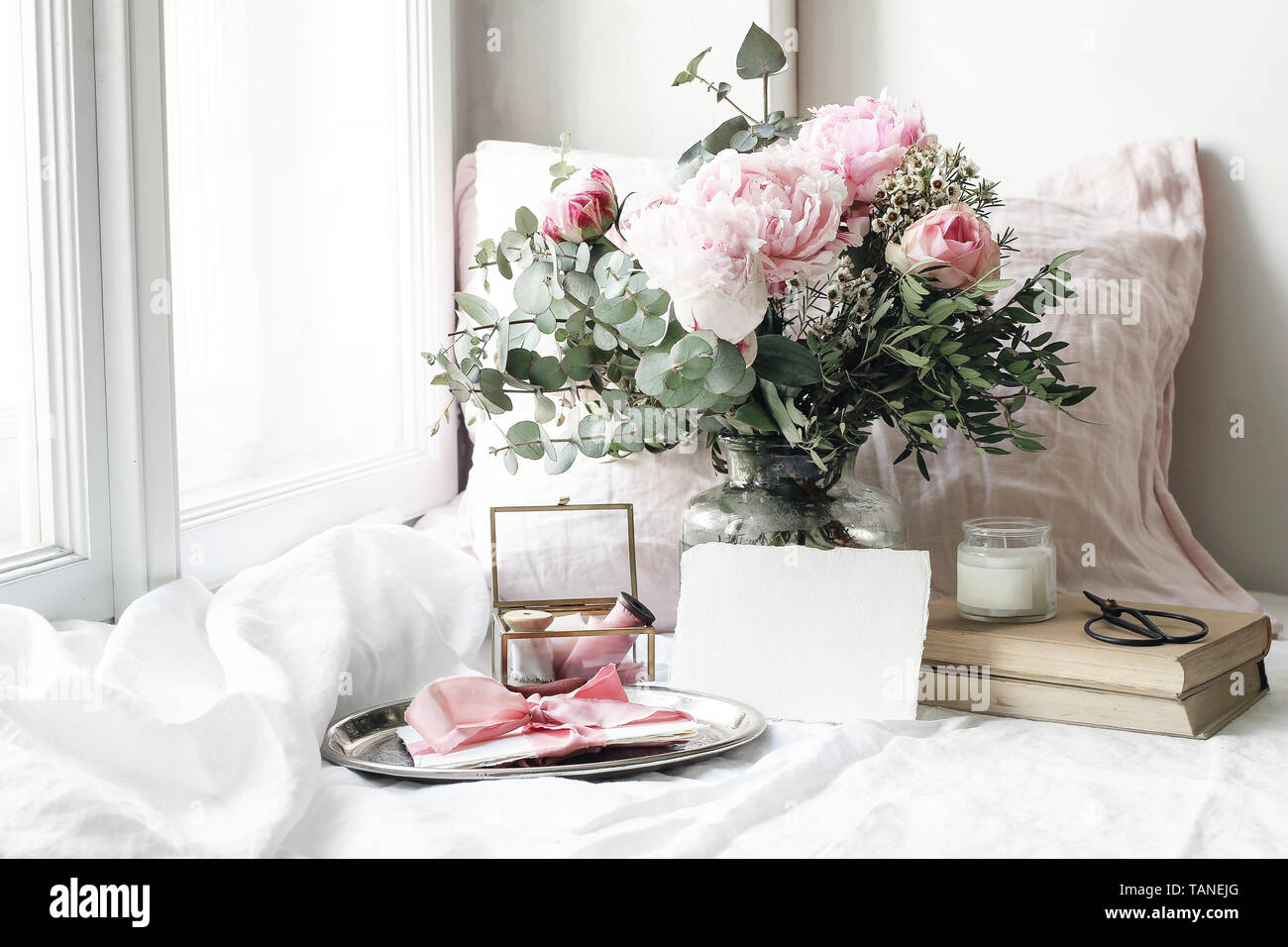 Frühling, Sommer Hochzeit Stillleben Szene. Leeres Papier Karte Mockup, alte Bücher und Bettwäsche Kissen an der Fensterbank. Vintage feminin blumige Komposition Stockfoto