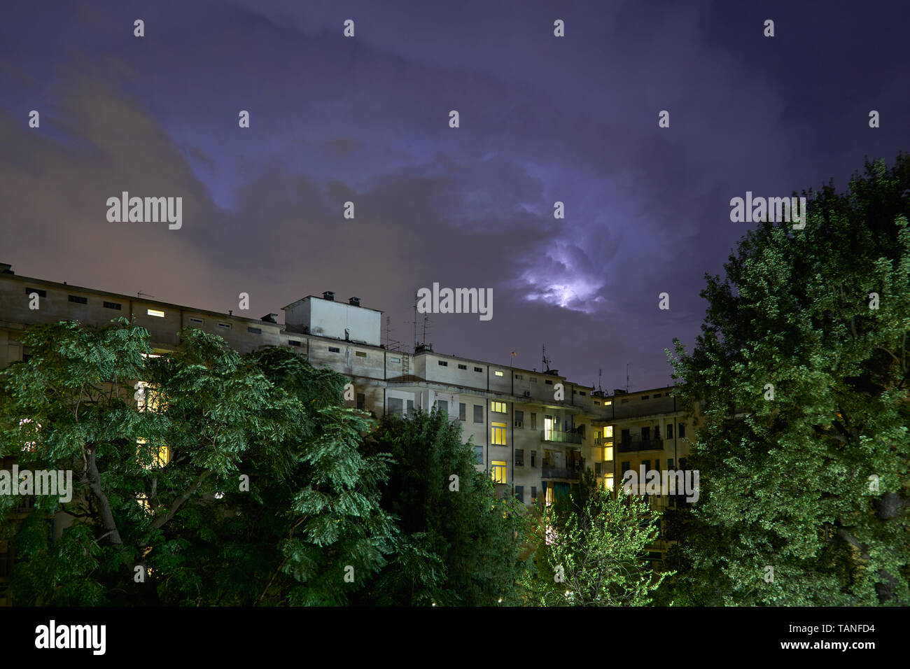 Gebäude und grüne Bäume bei Nacht, beleuchtete Himmel während eines Gewitters Stockfoto