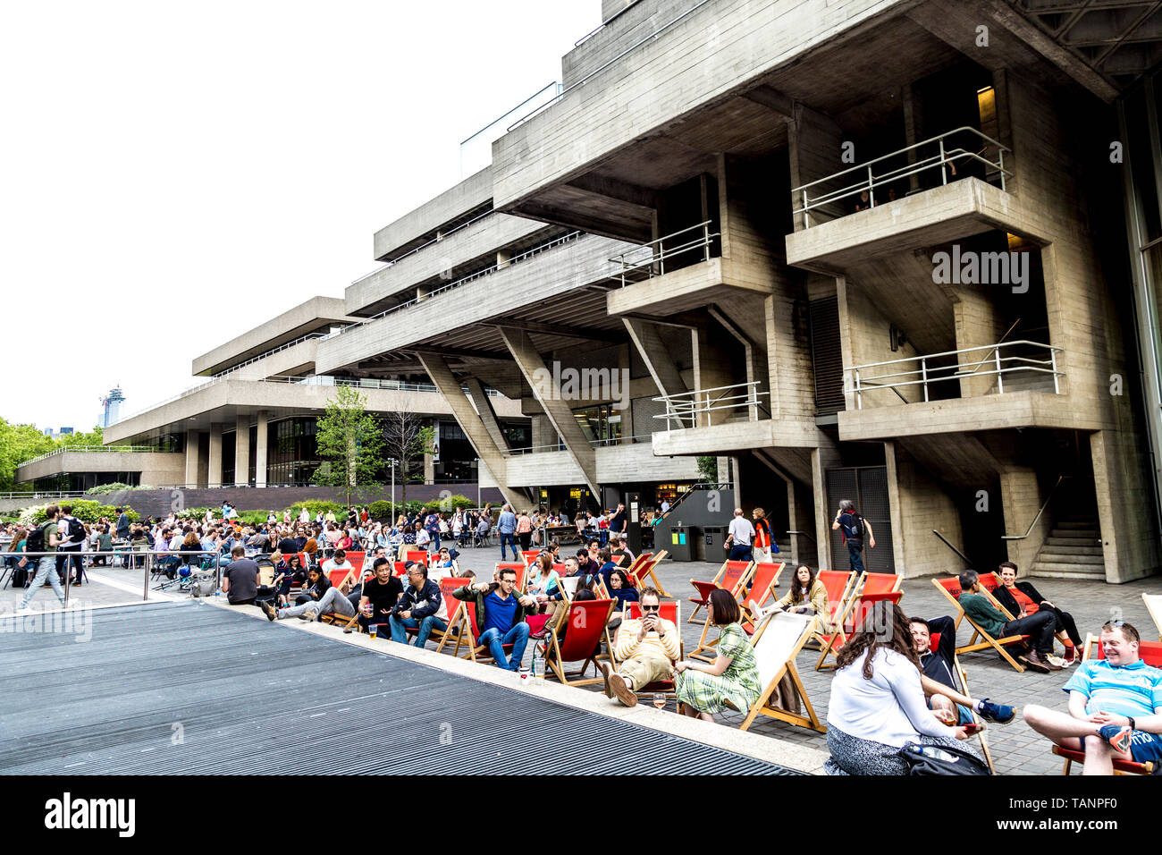 Menschen sitzen in Liegestühlen auf der Southbank vor dem National Theatre, London, UK Stockfoto