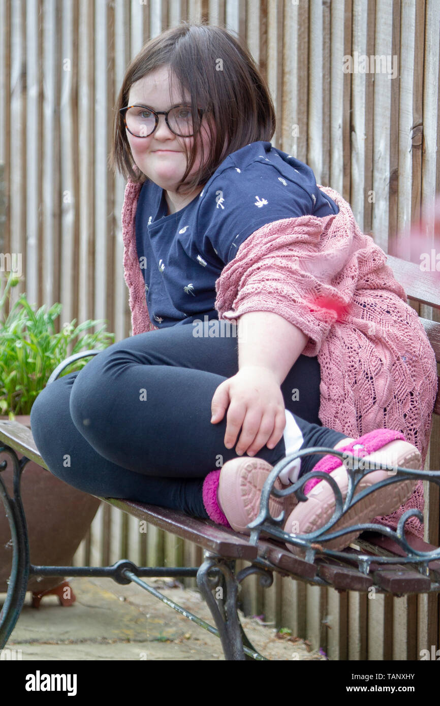 Mädchen mit Down-syndrom sitzen auf einer gartenbank Leben genießen und den Garten. Stockfoto