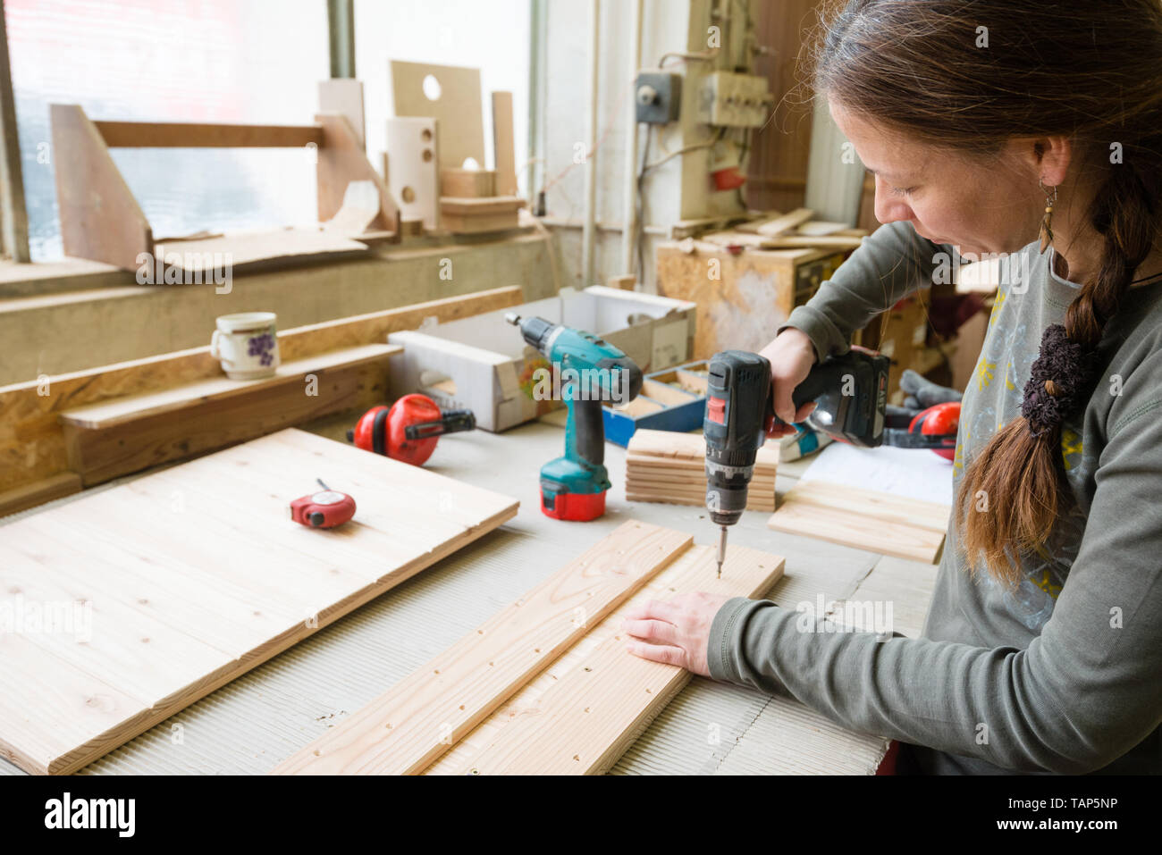 Junge Frau mit elektrischer Schraubenzieher auf ein Stück Holz in der Werkstatt Stockfoto