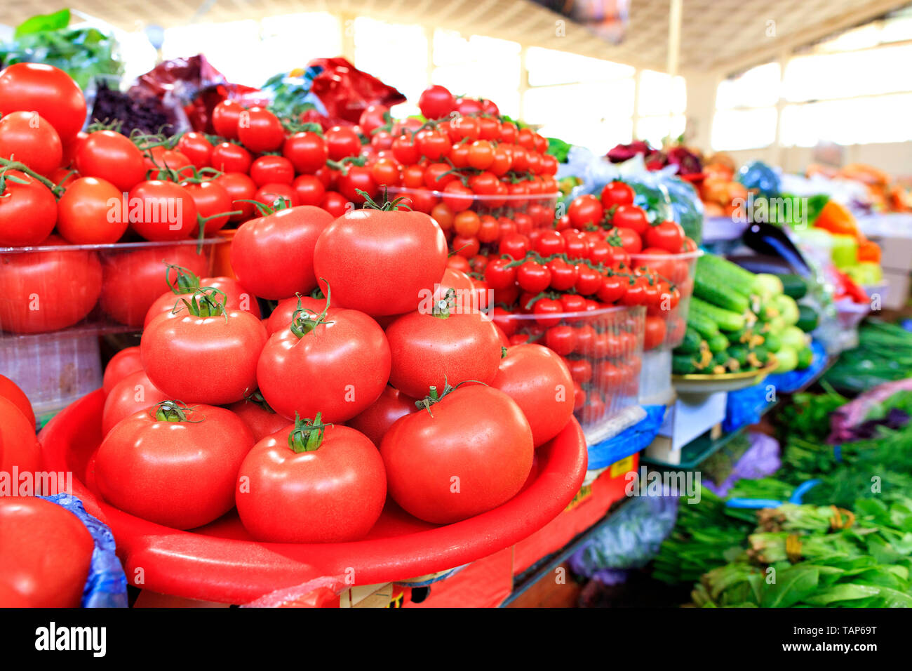 Verschiedene Sorten von reife rote Tomaten in den Hintergrund im Unscharfen von Gurken, Spinat und anderem Gemüse in die Fächer auf dem Markt Stockfoto