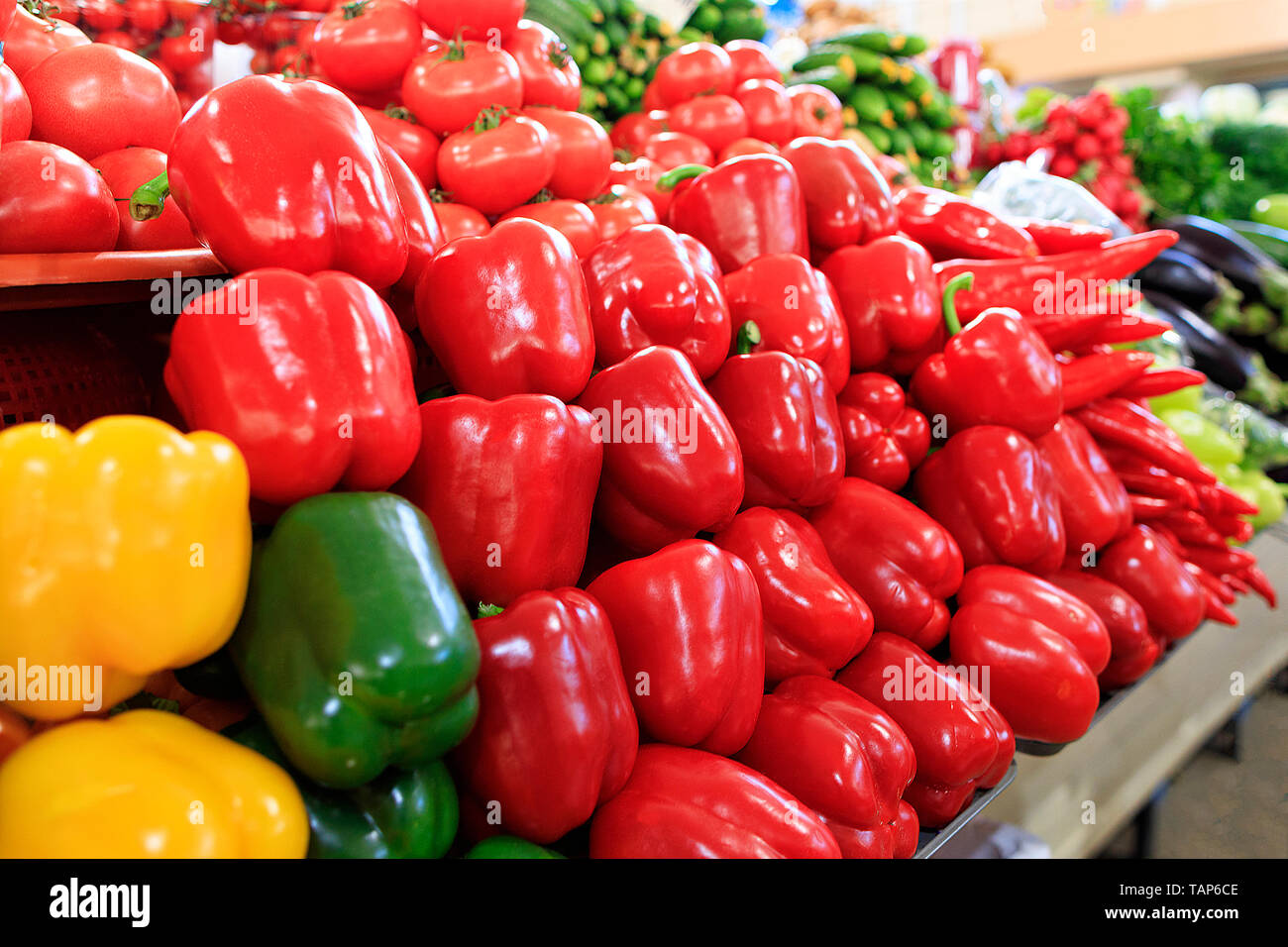 Verschiedene Sorten von rote, gelbe und grüne Paprika in den Hintergrund unscharf Gurken, Spinat und anderem Gemüse werden in Schalen auf der verkauft Stockfoto