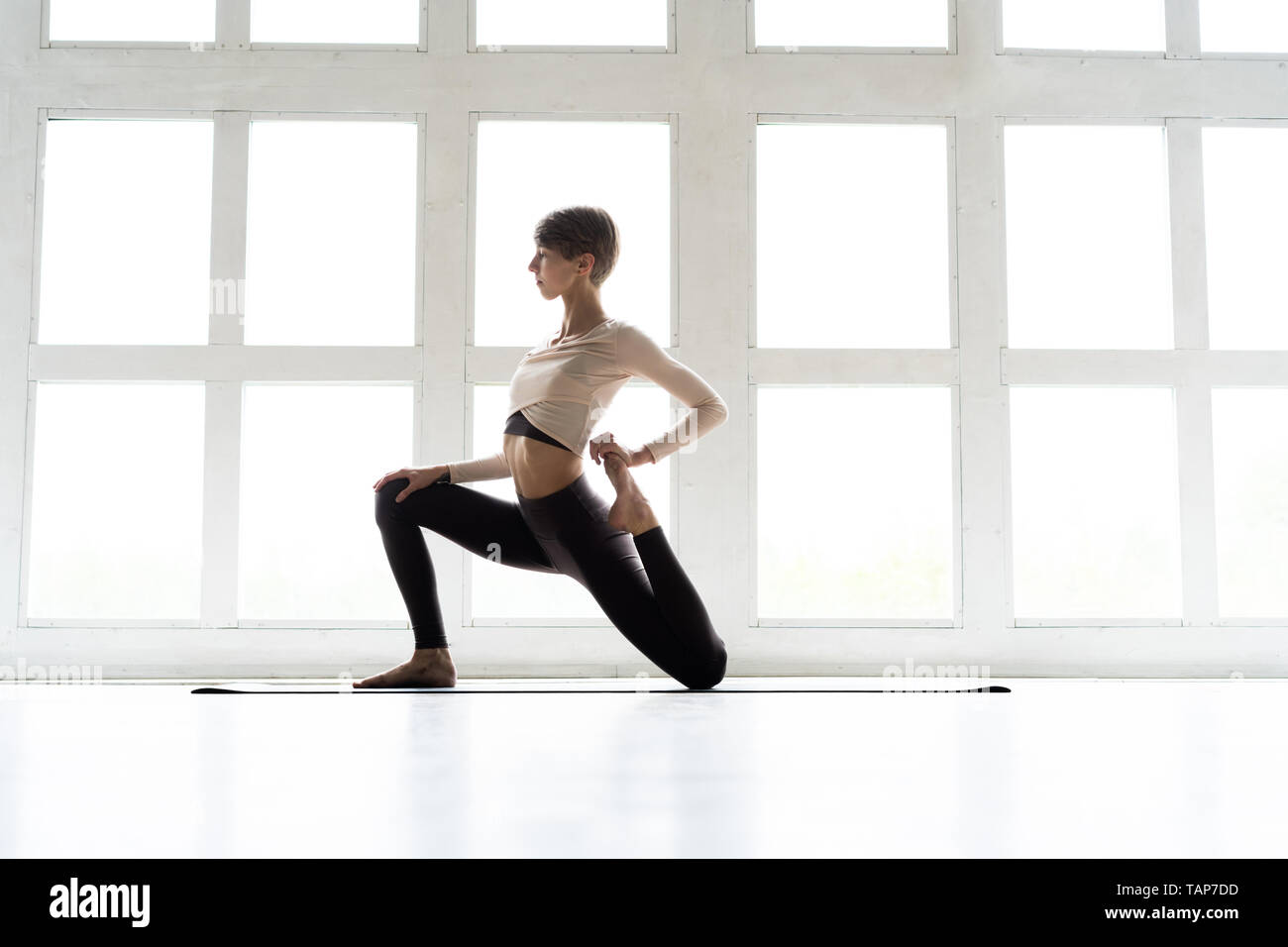 Junge attraktive Frau Üben Yoga, in Pferd Reiter Übung stehend, anjaneyasana darstellen, Arbeiten, Sportkleidung tragen, coole Urban Style Stockfoto