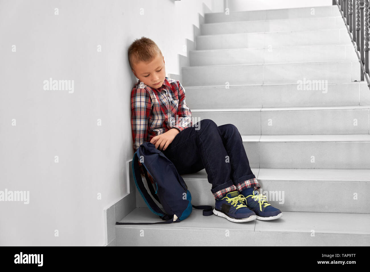 Einsam, depressiv Junge sitzt auf Treppe der Grundschule. Stattlich, müde und traurig Schüler tragen in kariertes Hemd und Jeans, suchen, denken. Stockfoto