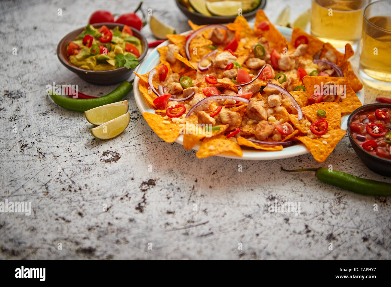 Mexikanischer Mais nacho würzige Chips mit geschmolzenem Käse serviert, Paprika, Tomaten, Bier und Salsas. Stockfoto