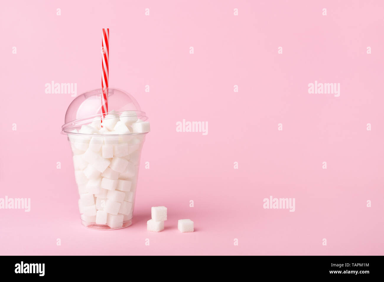 Schütteln Glas mit Stroh voller Würfel Zucker auf Pastell rosa Hintergrund. Ungesunde Ernährung Konzept. Minimal, Kopie, von der Seite. Stockfoto