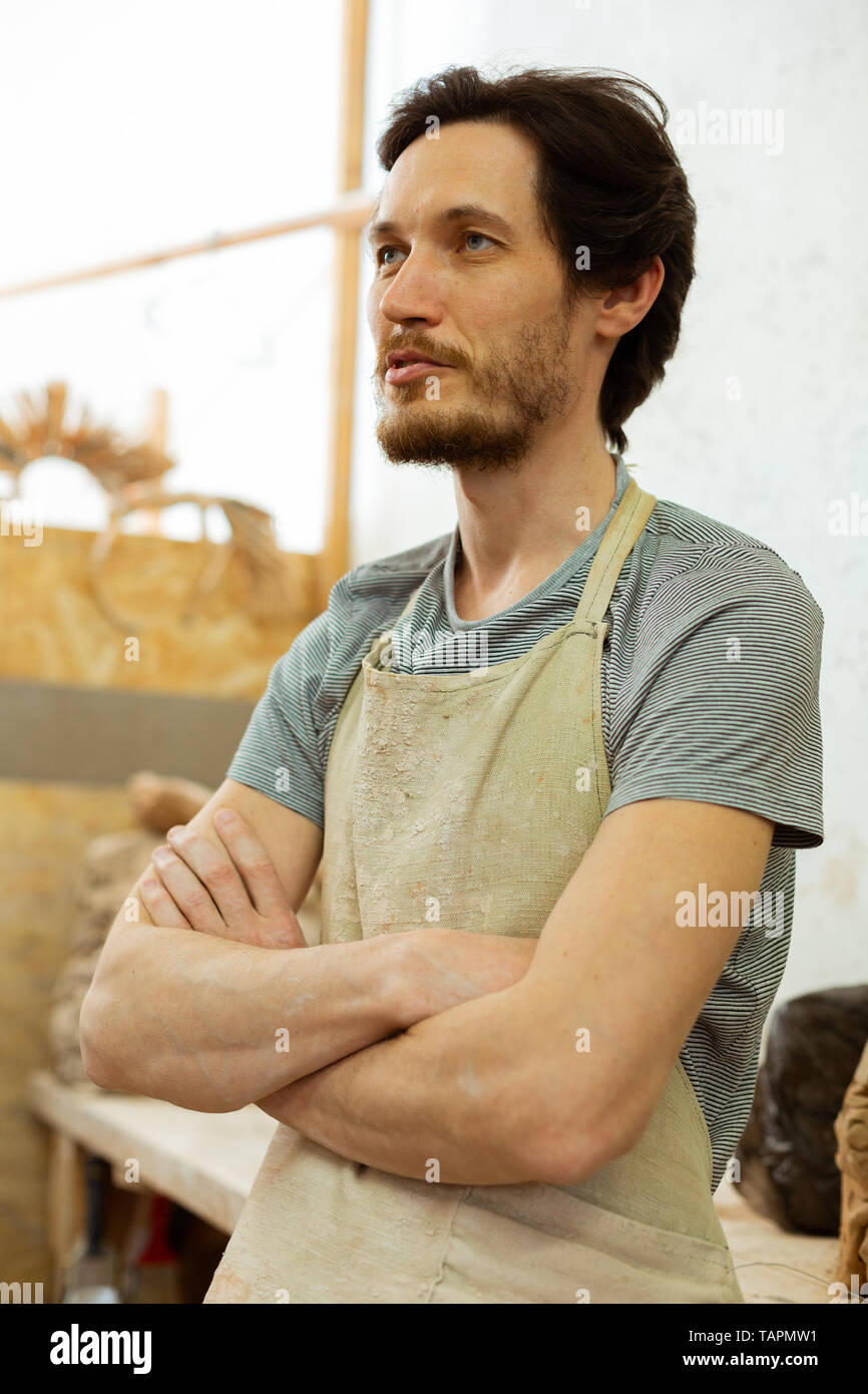 Der Aufenthalt in der Werkstatt. Kurzhaarige entschlossenen Mann in schmutzigen Schürze Vorbereitungen für den aktiven Tag in Keramik studio Stockfoto