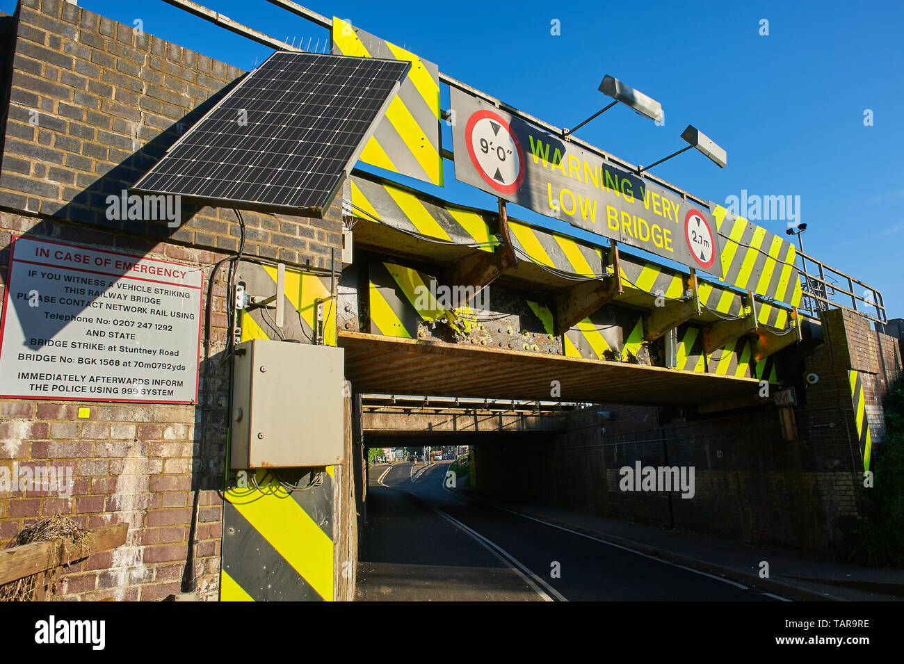 Niedrige Eisenbahnbrücke über die Straße, mit Warnzeichen, farbige Chevrons und Solar unterzeichnen. Stockfoto