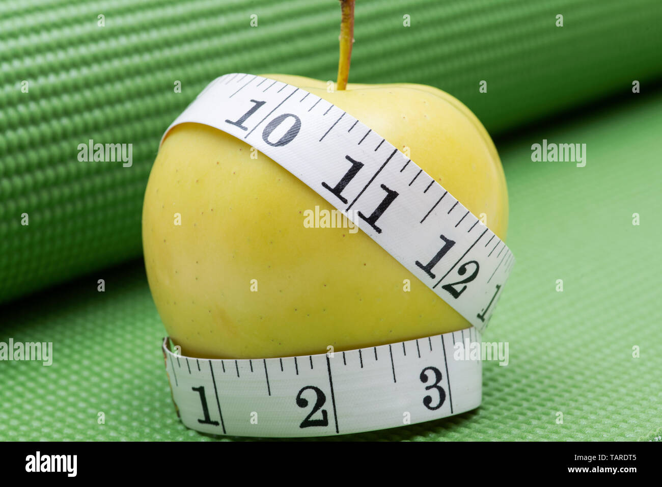 Gelber Apfel und weiches Vinyl Maßband auf Grün Yoga Matte. Stockfoto