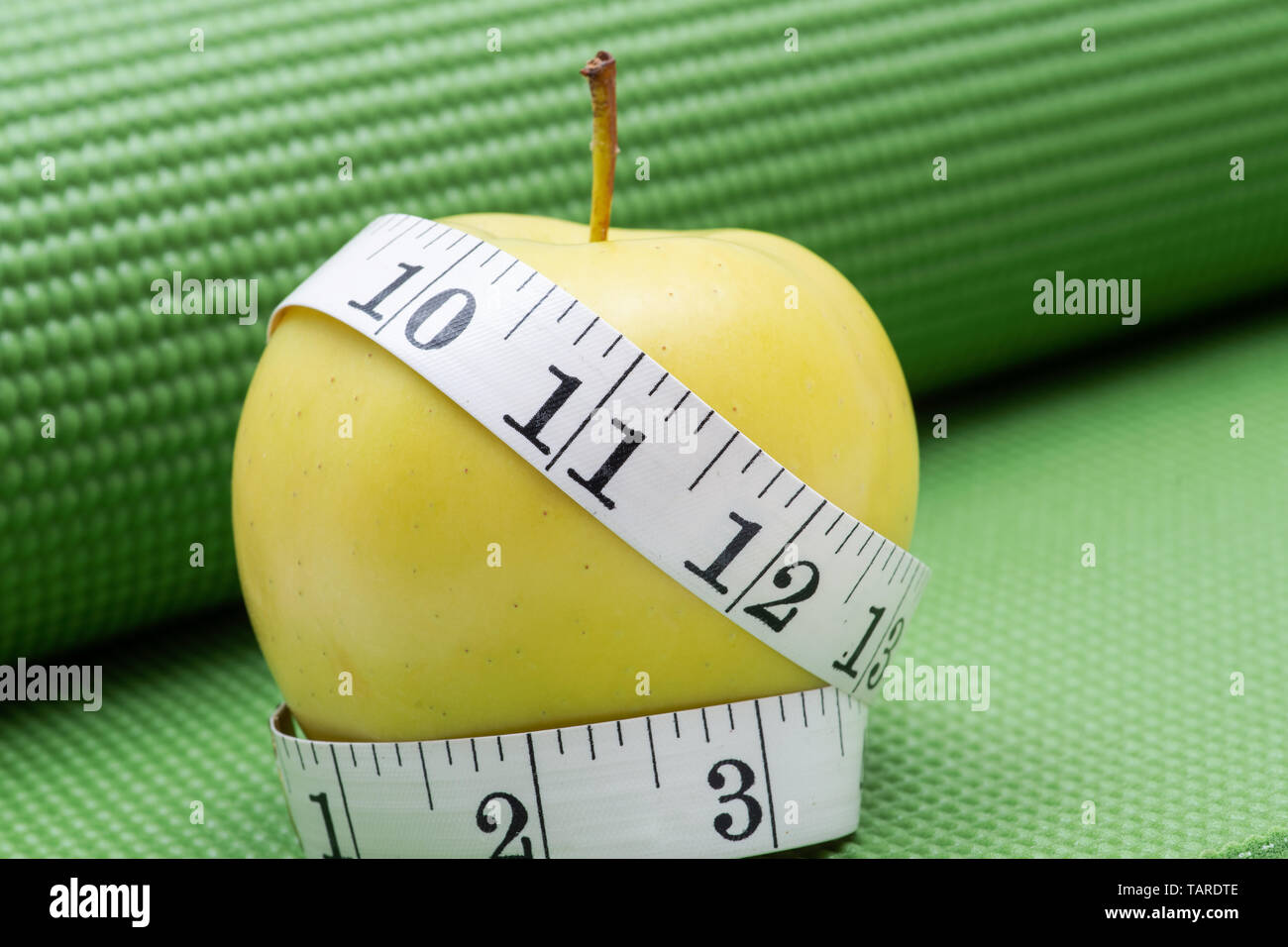 Gelber Apfel und weiches Vinyl Maßband auf Grün Yoga Matte. Stockfoto