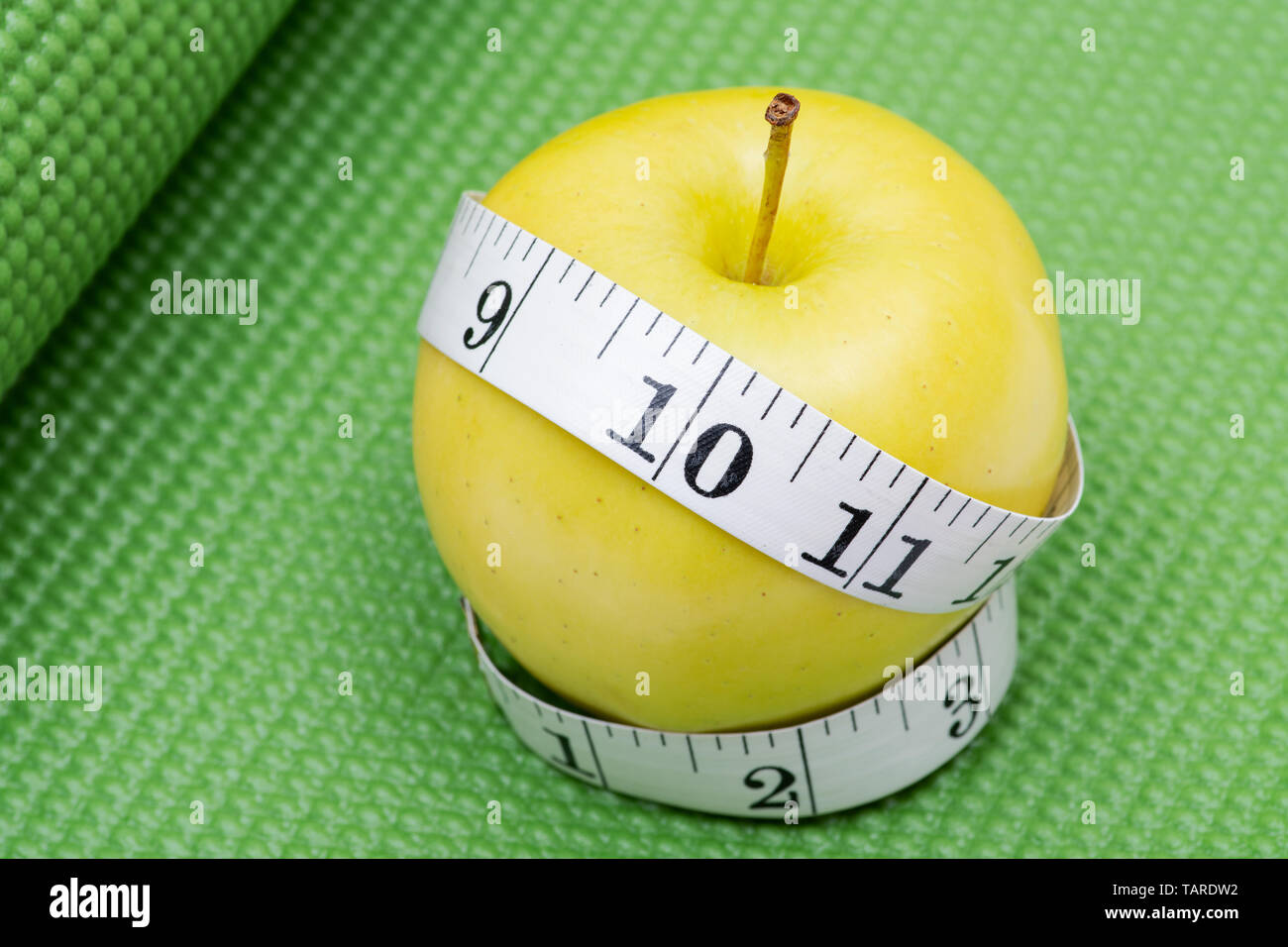 Gelber Apfel und weiches Vinyl Maßband auf Grün Yoga Matte. Stockfoto