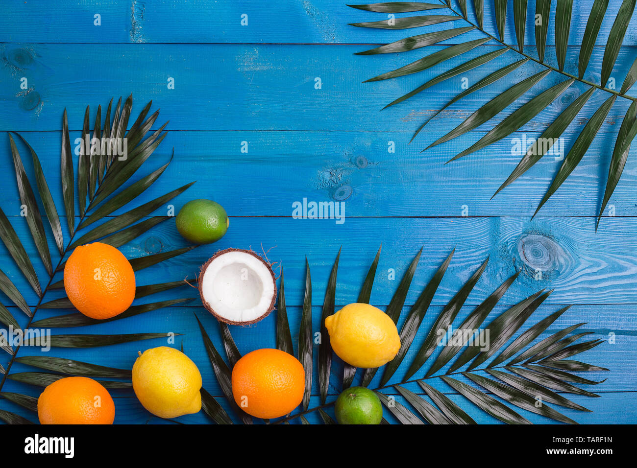 Verschiedene Früchte, grünen Blätter und Blumen auf blau Holztisch. Tropischer Sommer Hintergrund mit ein Raum für Text, Stockfoto