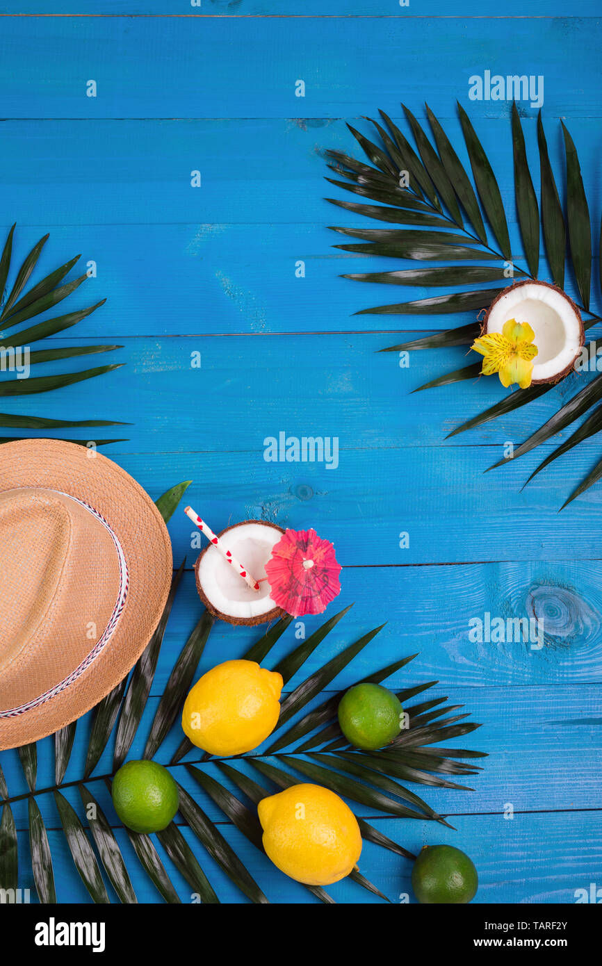 Tropischer Sommer Hintergrund mit Hut, Palmen, Zitronen, Limetten, Kokosnüsse auf Blau Holz- Hintergrund Stockfoto