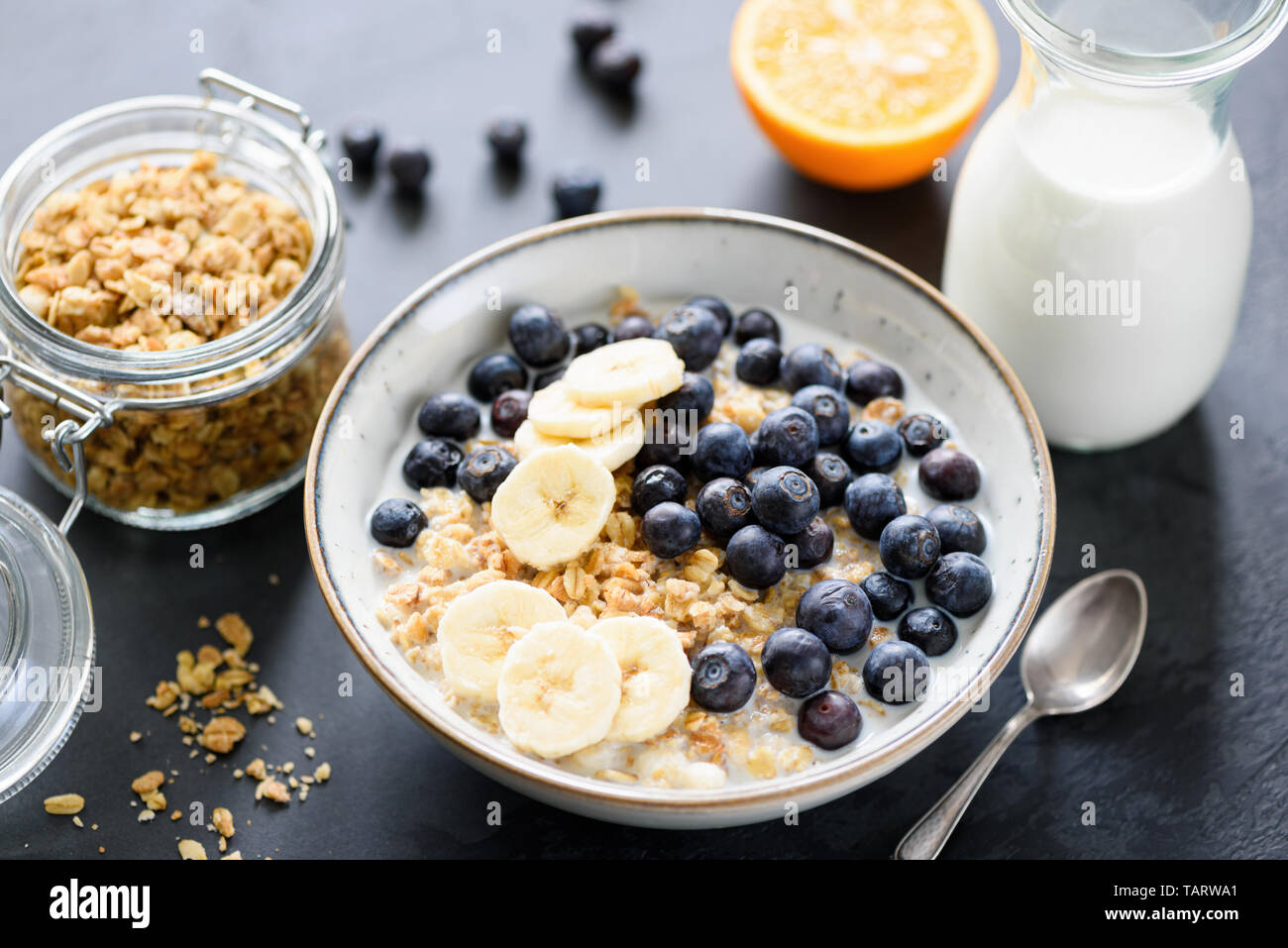 Schüssel Müsli mit Blaubeeren und Banane und Glas Milch auf dem Tisch. Gesundes Frühstück essen Stockfoto