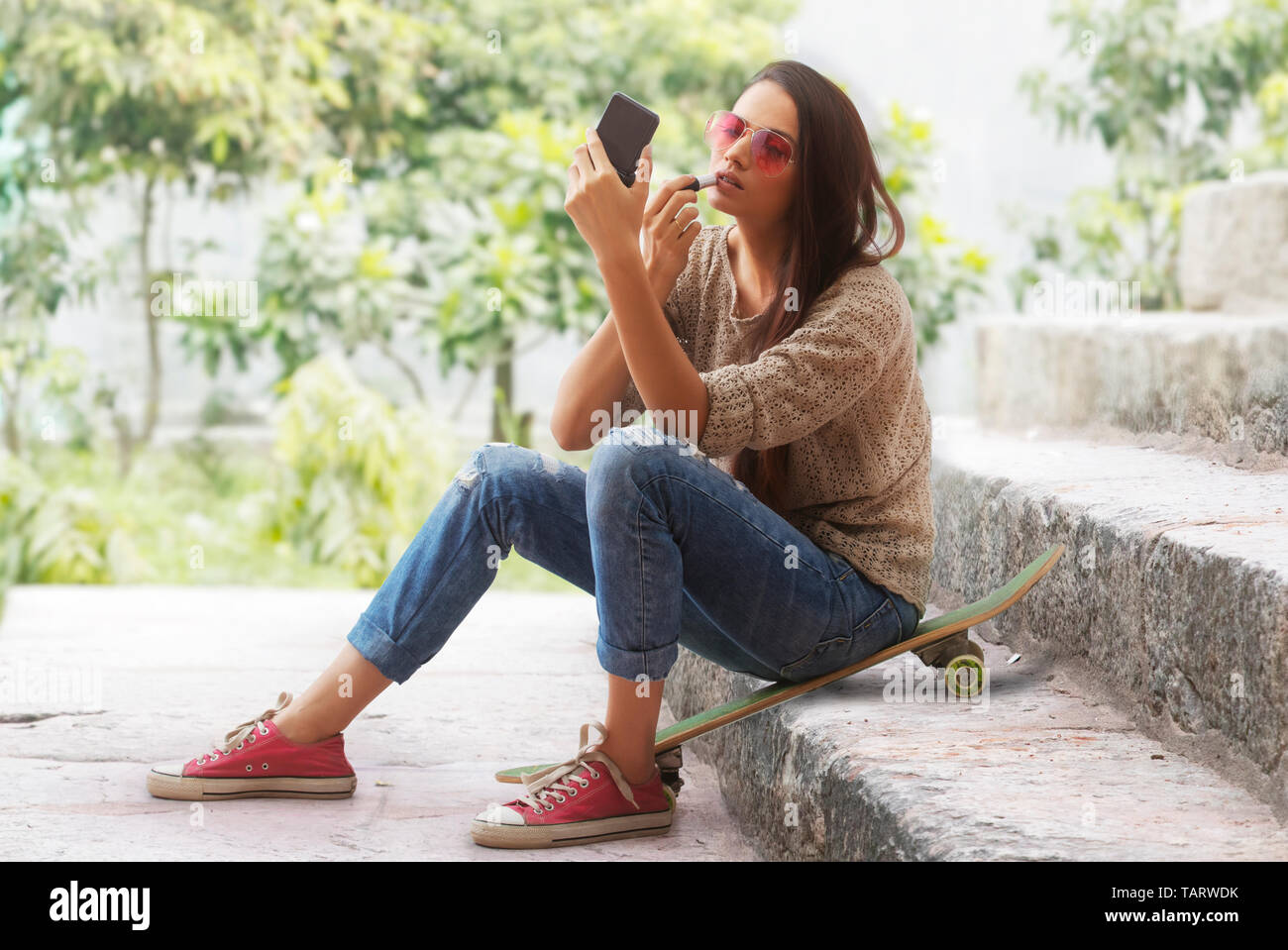 Frau sitzt auf einem Skateboard auf die Schritte der Anwendung Lippenstift Stockfoto