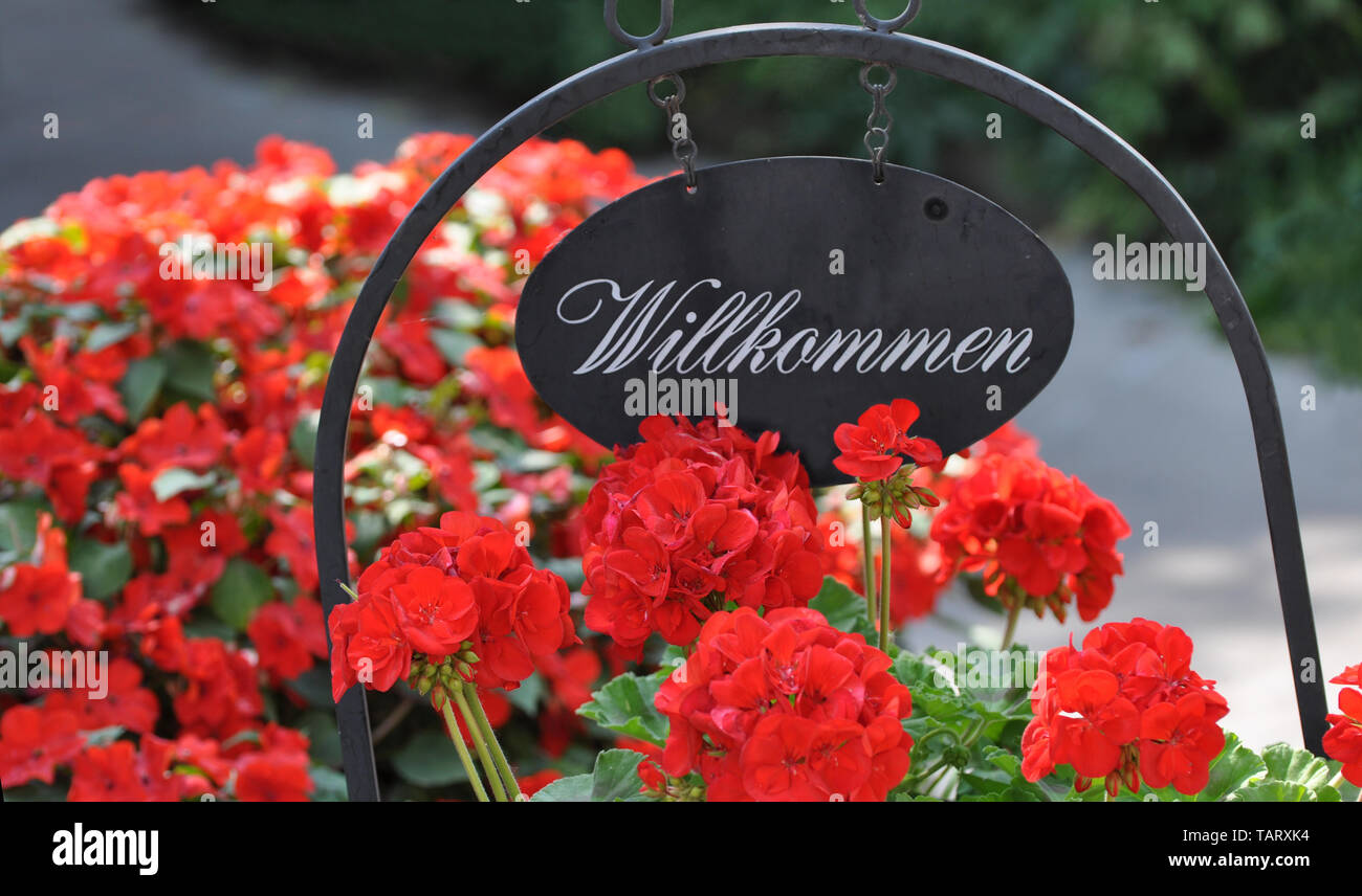In der Nähe der traditionellen österreichischen Metall Willkommen Schild mit roten Blüten. Deutsche Wort Welcome (Willkommen). Stockfoto