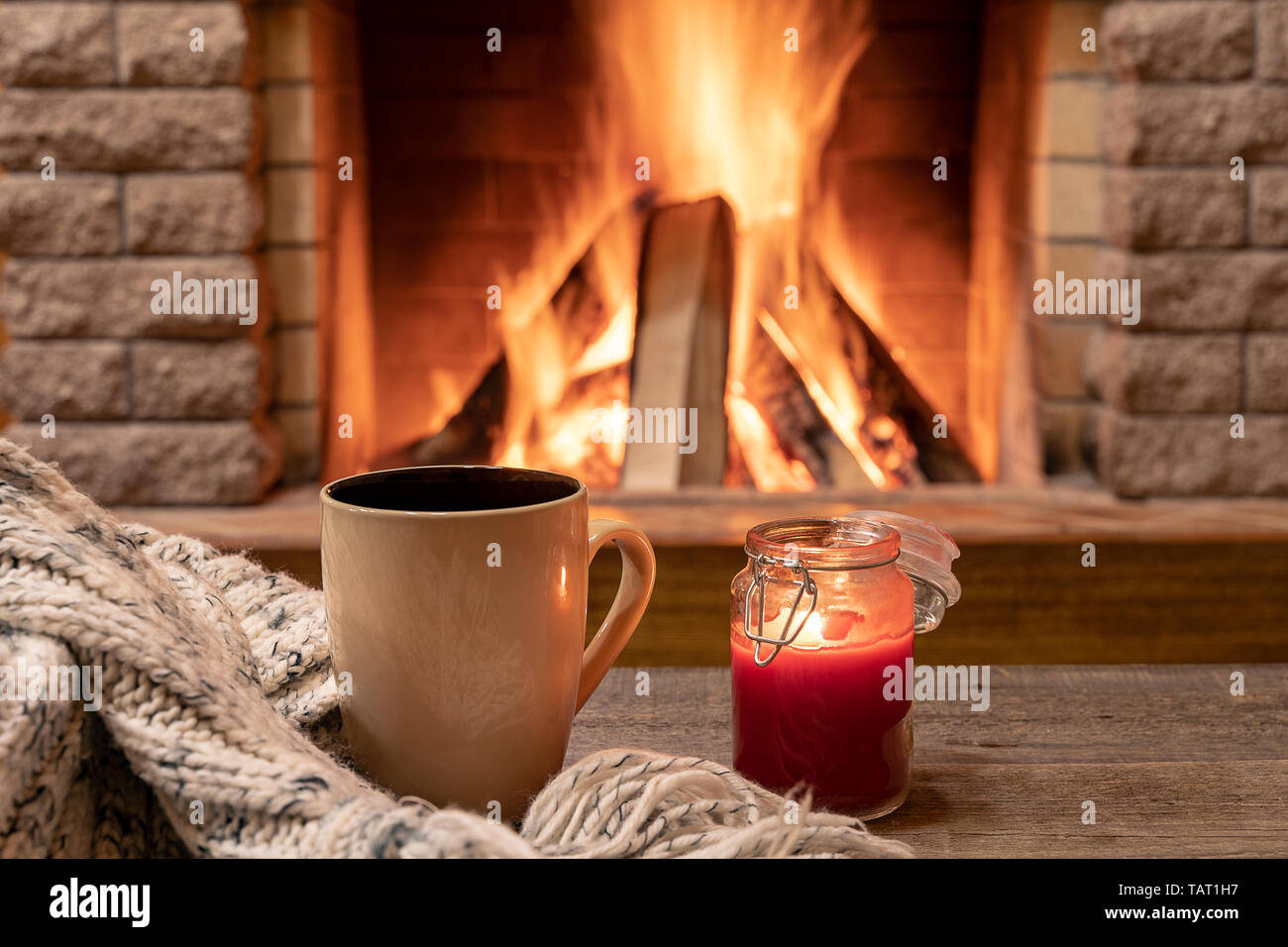Große Tasse mit heißem Tee und eine Kerze, Wolle Schal, in der Nähe der gemütlichen Kamin, im Landhaus, hygge, Home sweet home. Stockfoto
