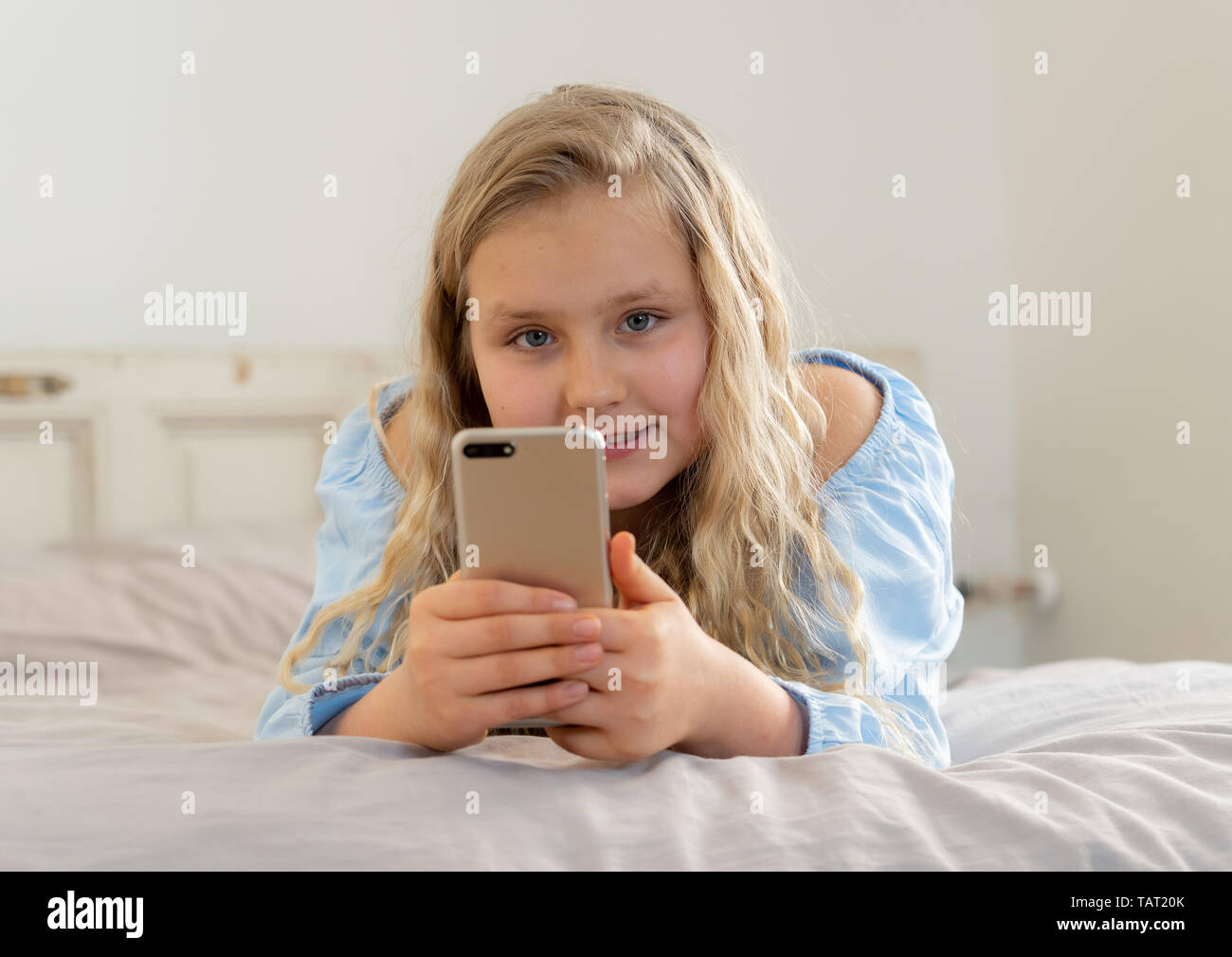 Schöne blonde glücklichen kleinen Mädchen spielen auf dem Handy. Niedlichen Kind im Internet mit Smartphone social media App im Bett zu Hause liegen zu plaudern. Stockfoto