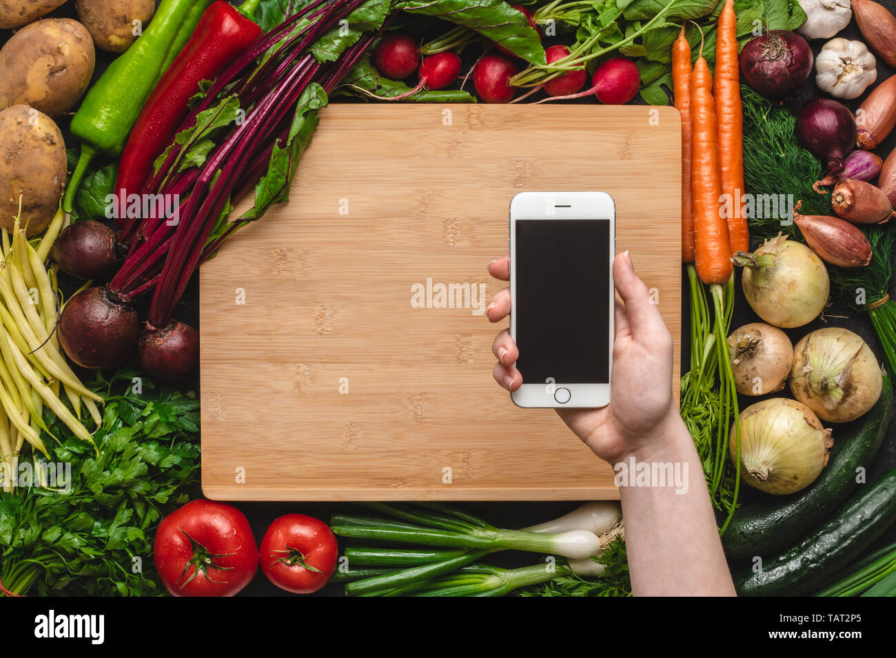 Hand mit Smartphone über Frisches Bio-Gemüse Hintergrund. Veganes Essen Rezepte. Stockfoto