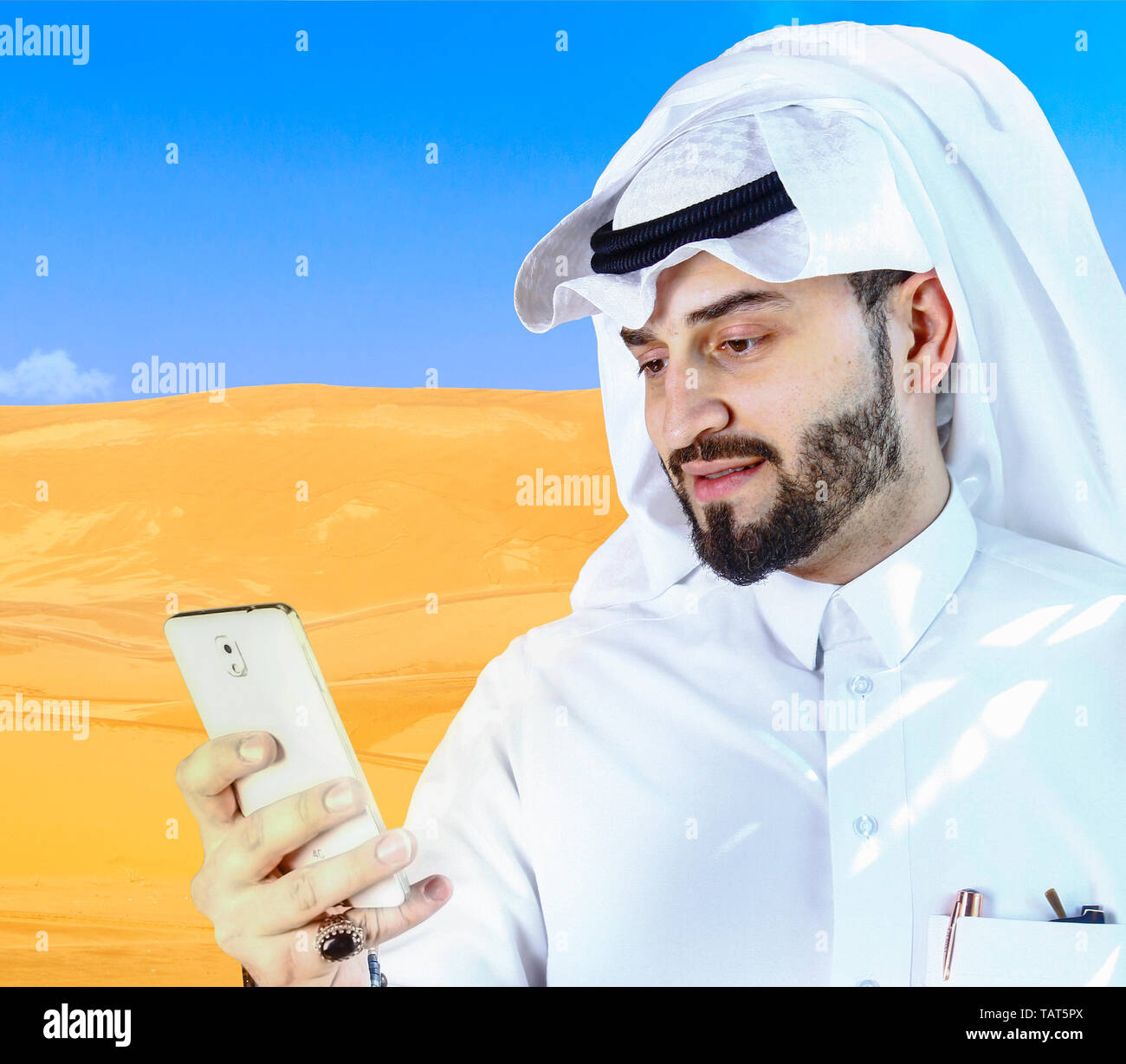 Ein Araber, der ein Handy benutzt, mit Wüstenhintergrund. Stockfoto