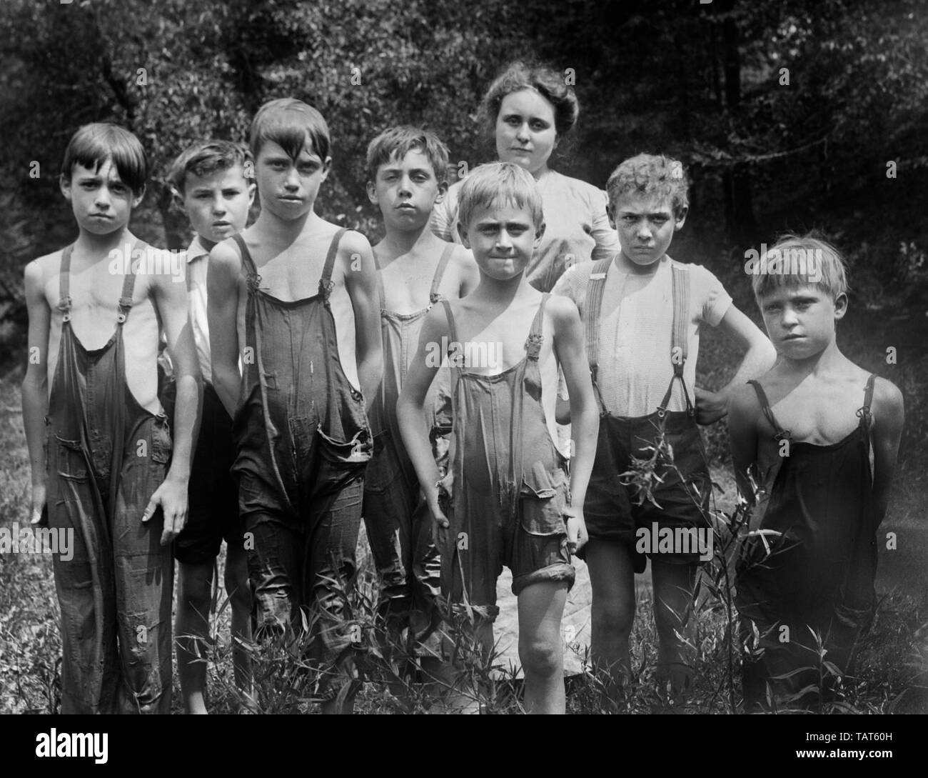 Eine Mutter steht mit einer Gruppe von Schulpflichtigen jungen Nass tragen Overalls, Ca. 1930. Stockfoto