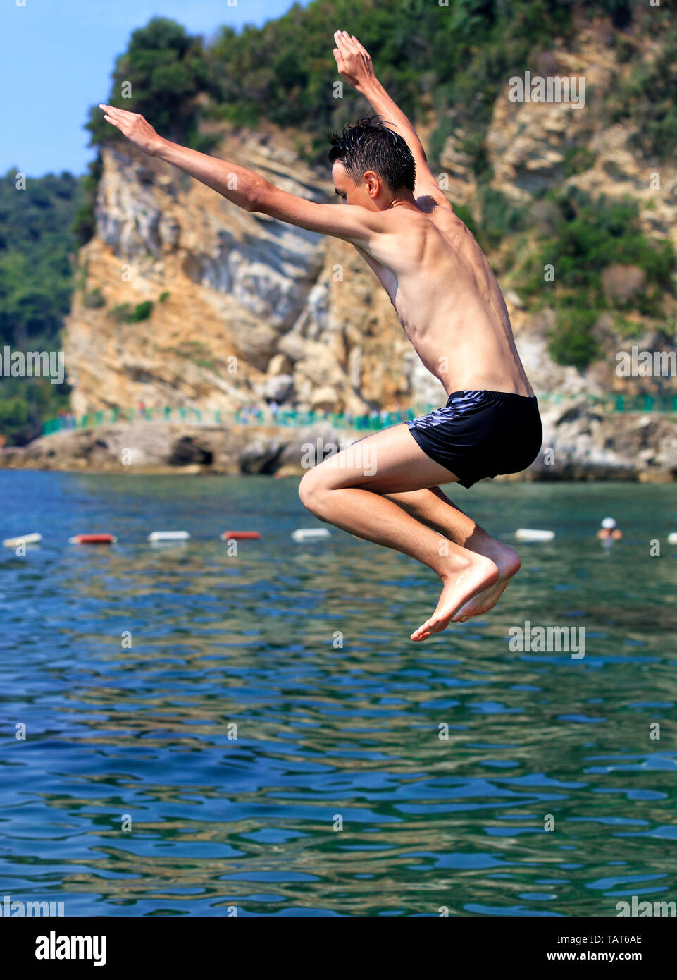 Brave Teenager springt von einer Klippe ins Meer vor dem Hintergrund der defensive Küste Bojen Stockfoto