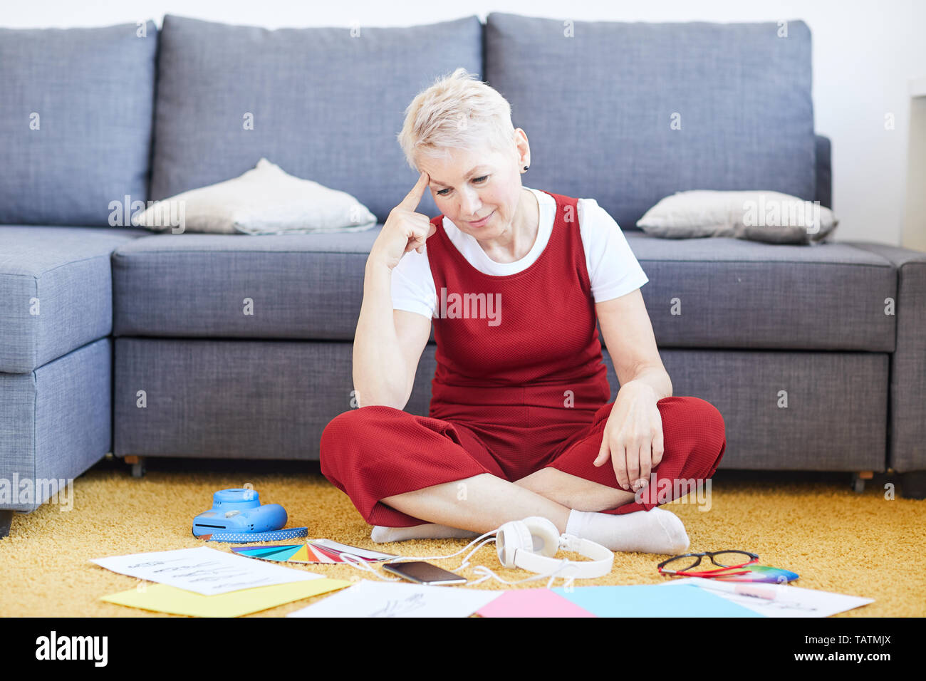 Hübsche blonde Frau in casualwear sitzen auf dem Boden von Couch, während Sie durch Art und Modelle für die neue Kollektion Stockfoto