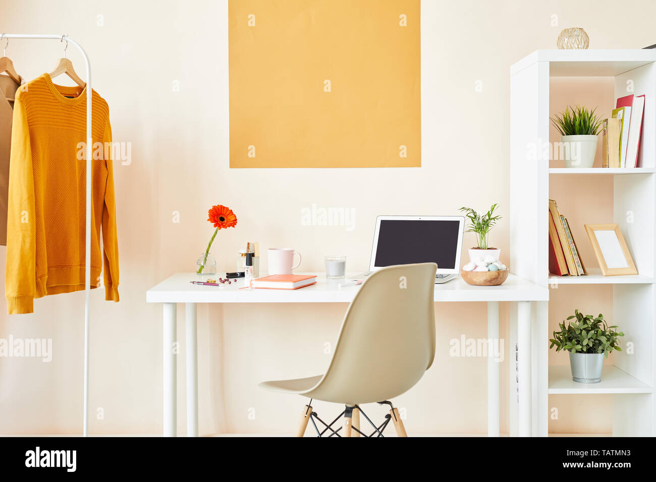 Arbeitsplatz für kreative Mitarbeiter oder Designer mit Schreibtisch, an der Wand, weiß Stuhl, Möbel mit Material- und Casualwear auf Kleiderbügeln Stockfoto