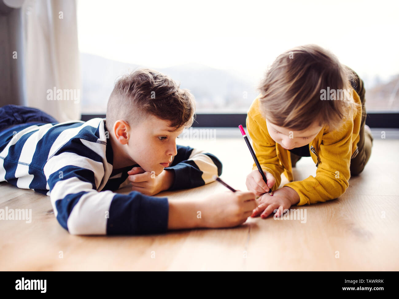 Zwei glückliche Kinder liegen auf dem Boden in Innenräumen zu Hause, Zeichnung. Stockfoto