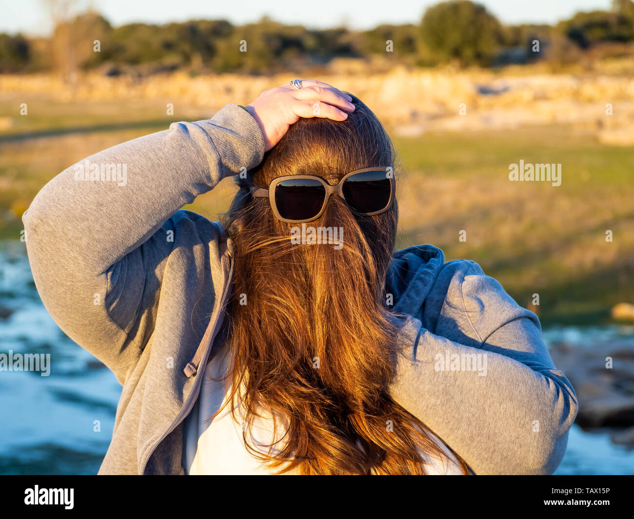 Eine kurvige Frau, die lustige Gesten mit Haar vor seinem Gesicht und Sonnenbrille Stockfoto