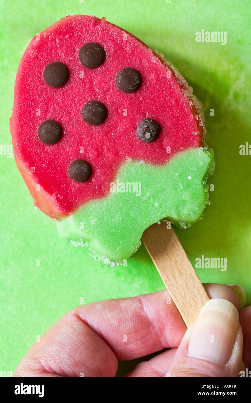 Holding Rowntrees Erdbeer Eis am Stiel auf grün gemusterten Hintergrund-set Erdbeere und Kiwi Wassereis mit Schokoladegeschmack Stücke Stockfoto