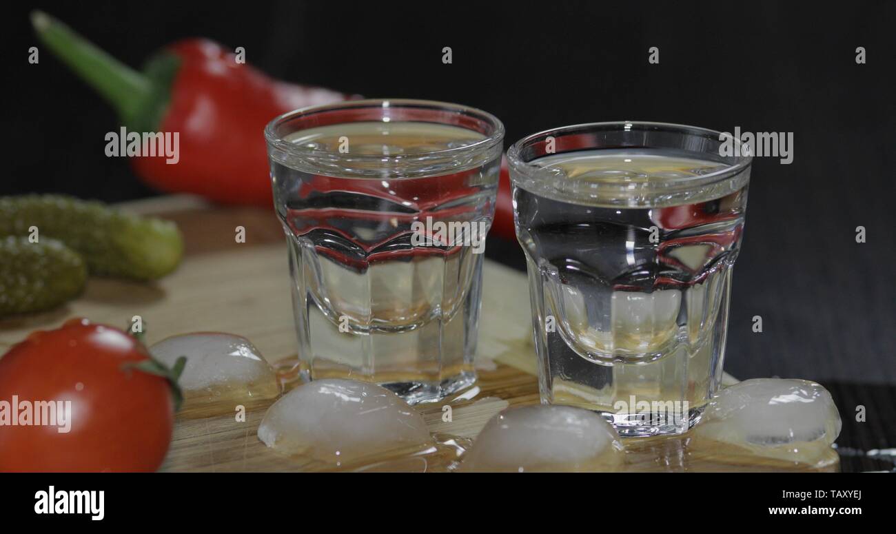 Zwei Schüsse von Wodka im Glas mit Eiswürfeln, Kirschtomaten, marinierten Gurken, Pfeffer auf dem Tisch. Stockfoto