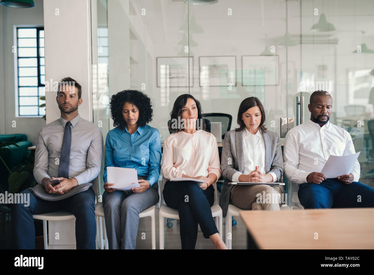 Gruppe der Verschiedenen Bewerber sitzen auf Stühlen außerhalb eines Büros warten auf Ihre interview Termine Stockfoto