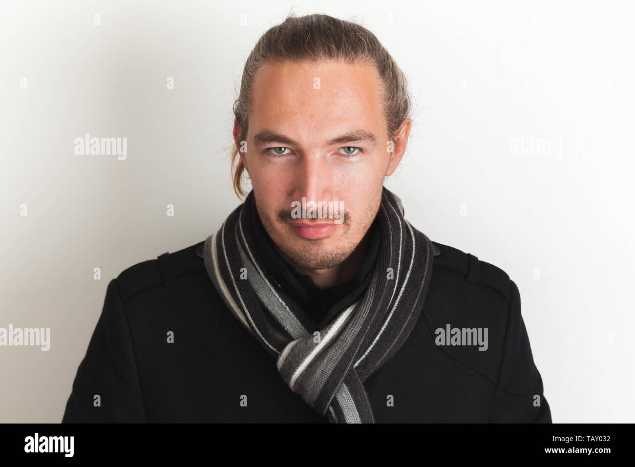 Junge Erwachsene asiatischer Mann im schwarzen Mantel und Wollschal steht über weiße Wand im Hintergrund. In der Nähe von Studio Portrait Stockfoto