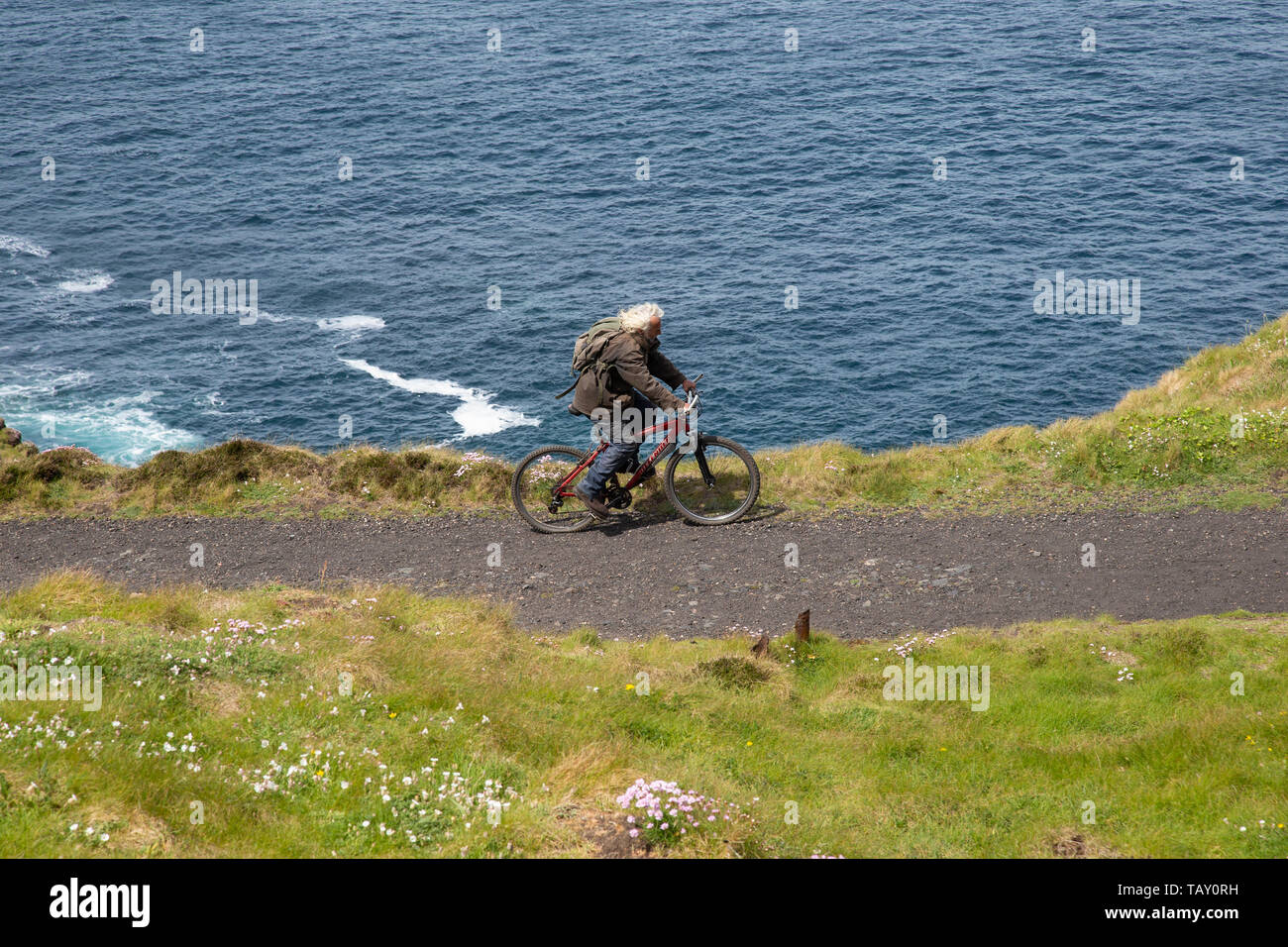 Langhaarige männliche Radfahrer reiten entlang der nördlichen Küstengebiet Kiesweg in Cornwall in der Nähe der steilen Klippe fallen in den Atlantischen Ozean Stockfoto