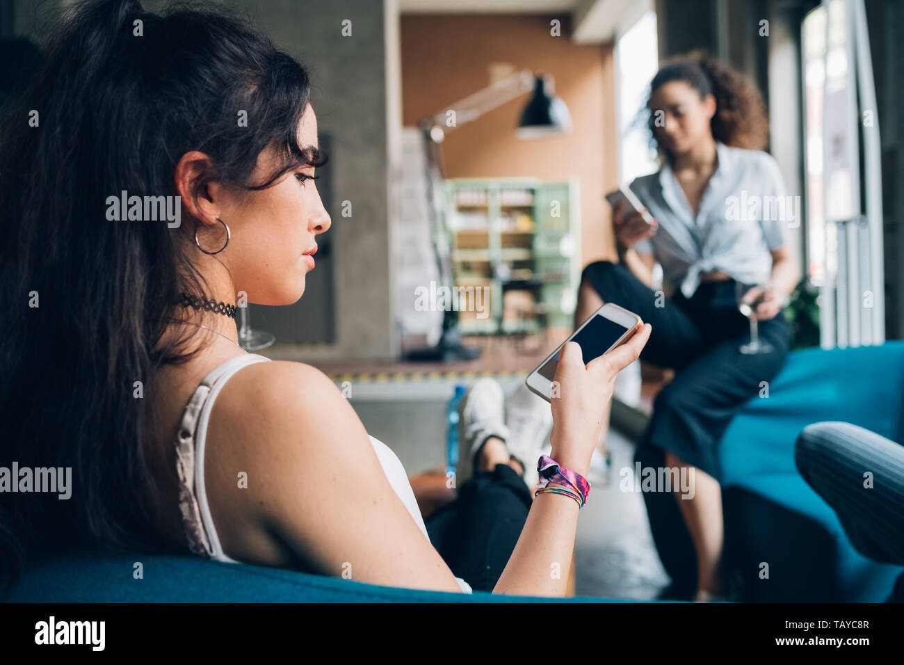 Zwei junge Frauen sitzen im modernen Pub und mit Smartphone - Technologie, heiter, Kommunikation Stockfoto